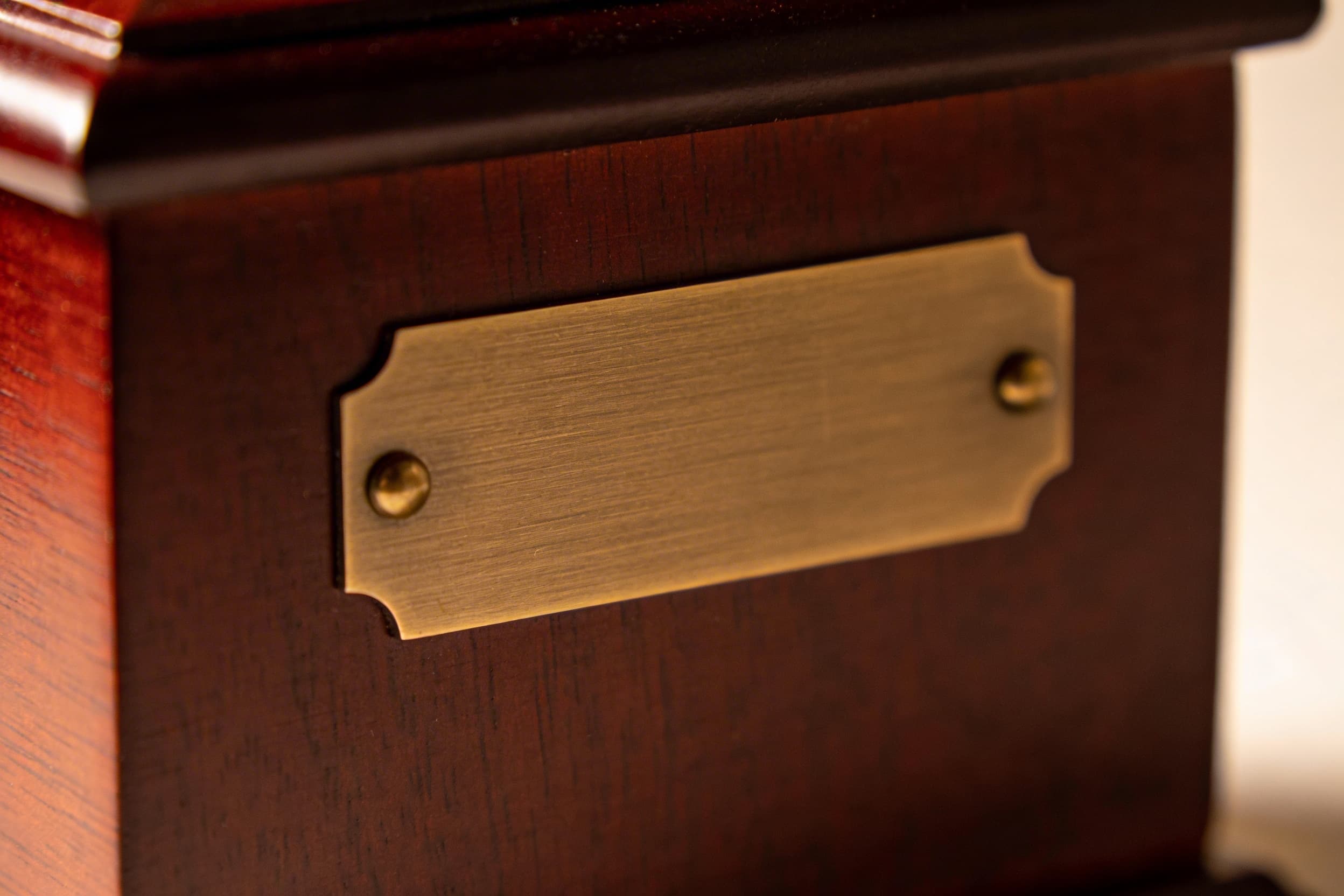 Close-up of an engraved cremation urn nameplate showing delicate serif lettering on a brushed bronze surface
