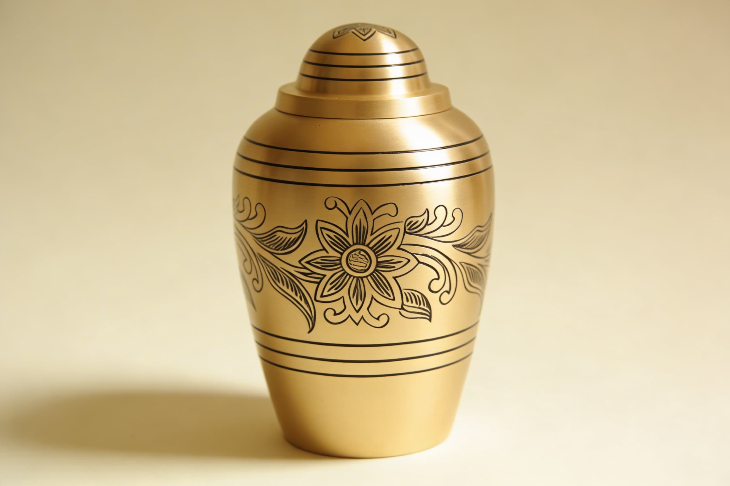 A polished brass cremation urn with a threaded lid, displayed against a soft neutral background