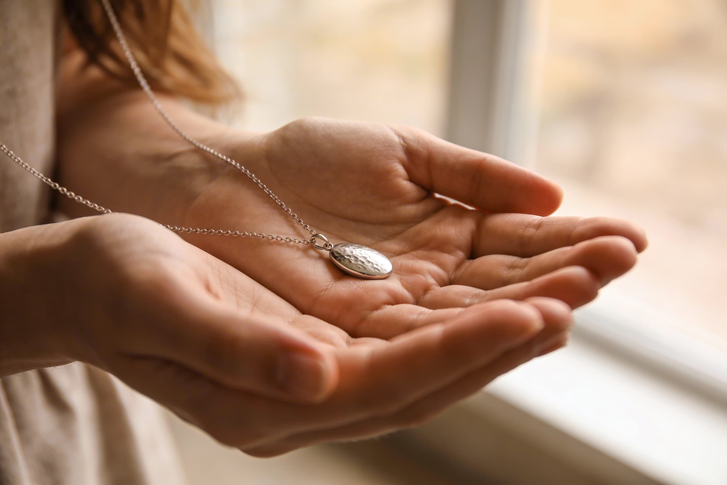 A small cremation pendant on a chain be held by a woman in her open hands