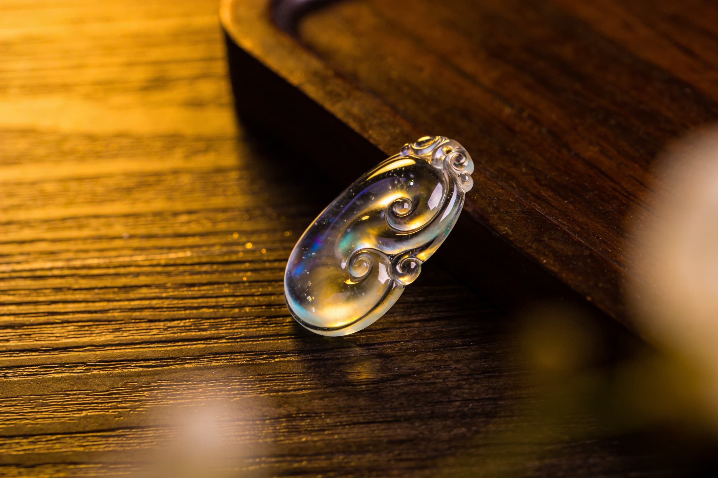 A glass cremation pendant in cobalt blue and clear glass displayed on a dark wood jewelry box, soft warm light highlighting the suspended white flecks inside