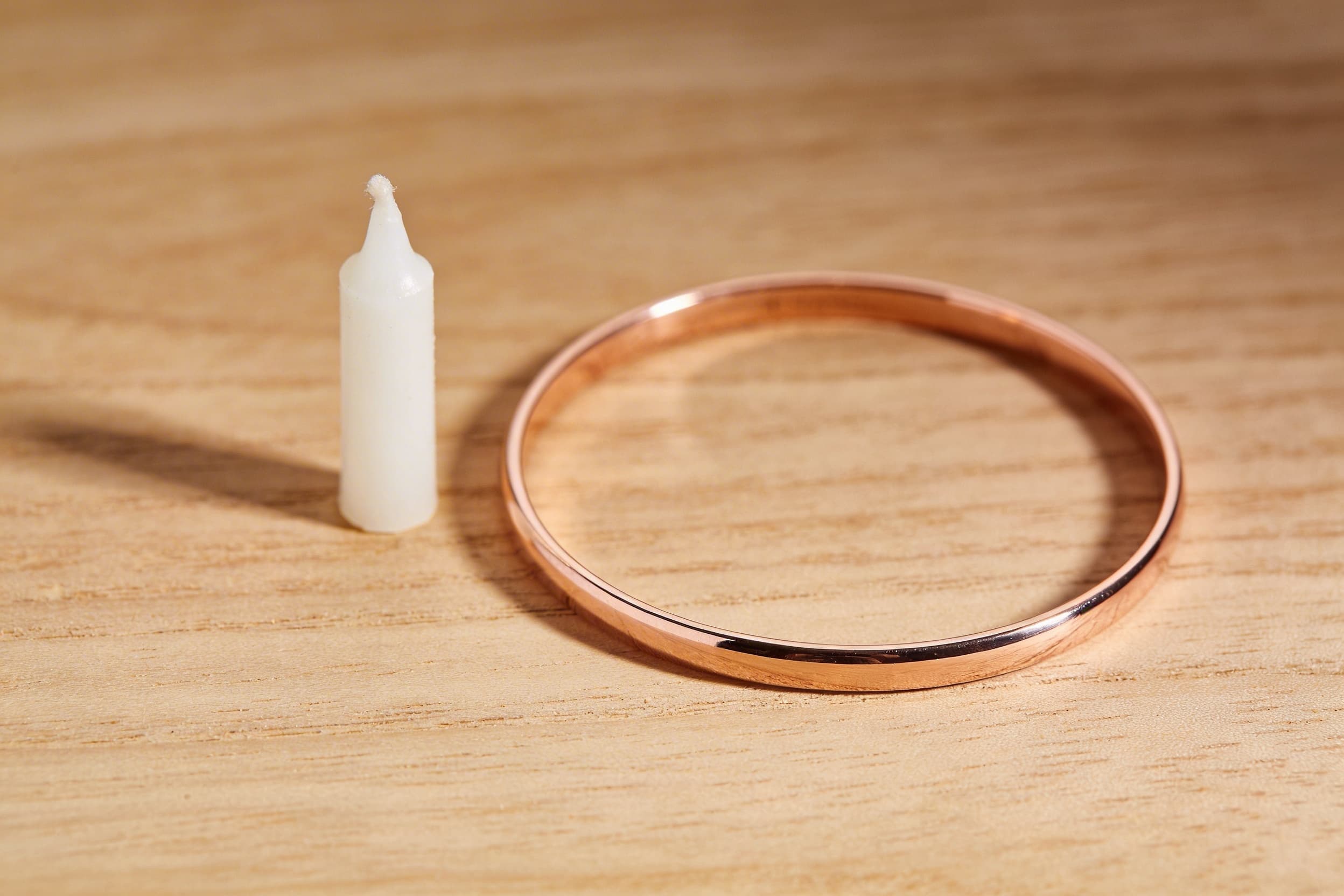 A rose gold cremation bangle bracelet resting on a wooden surface beside a small white candle