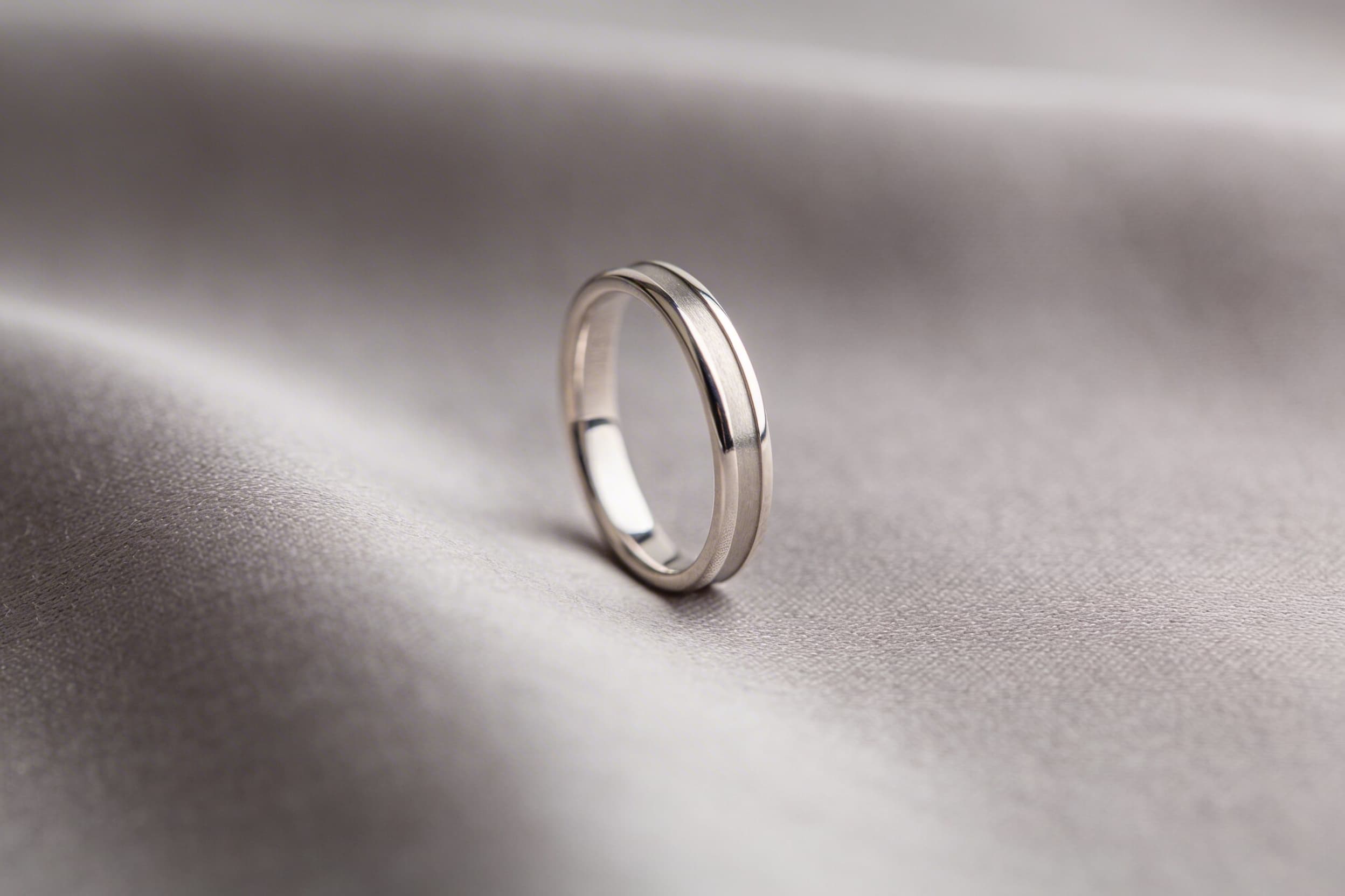 A delicate sterling silver cremation ring displayed on a light gray fabric surface with soft natural light