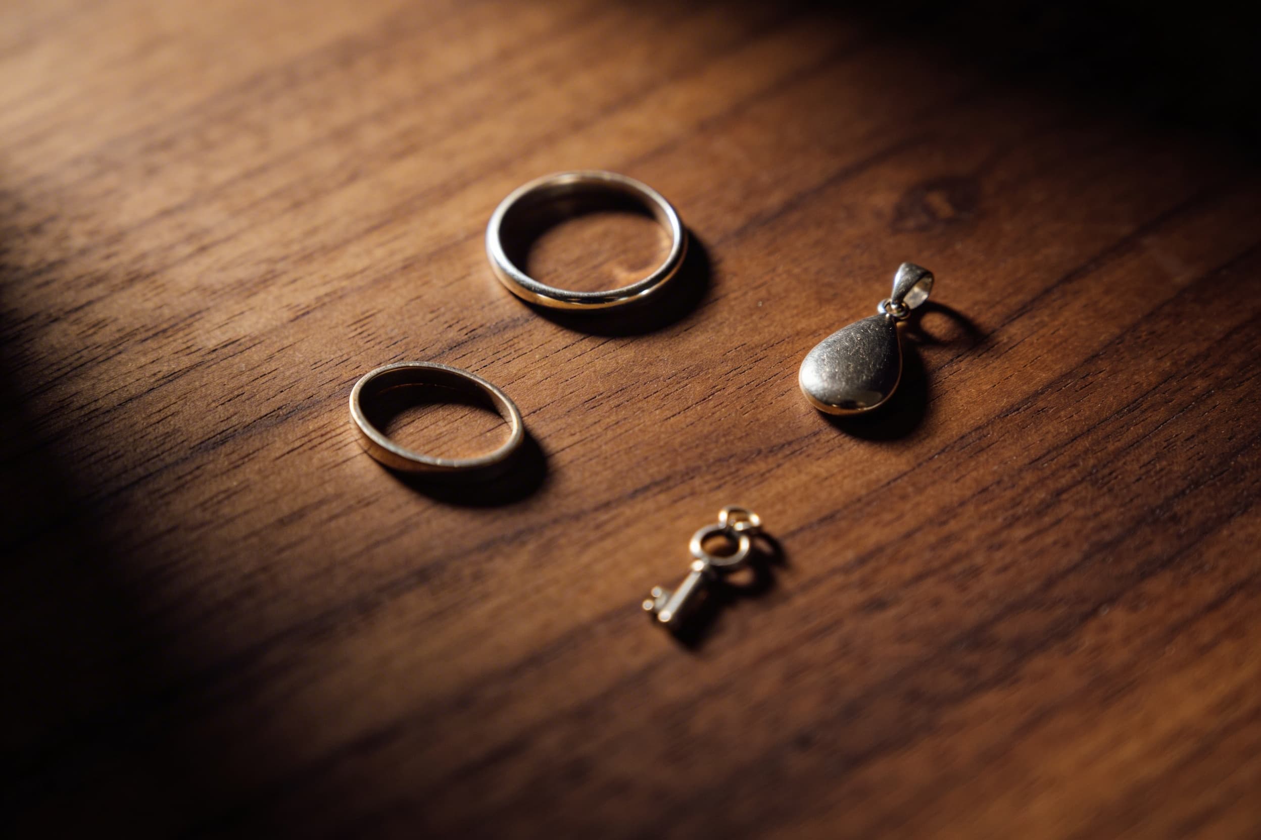 A flat lay of varied cremation jewelry styles โ a ring, pendant, small bracelet, and keychain โ arranged on dark wood with soft side lighting