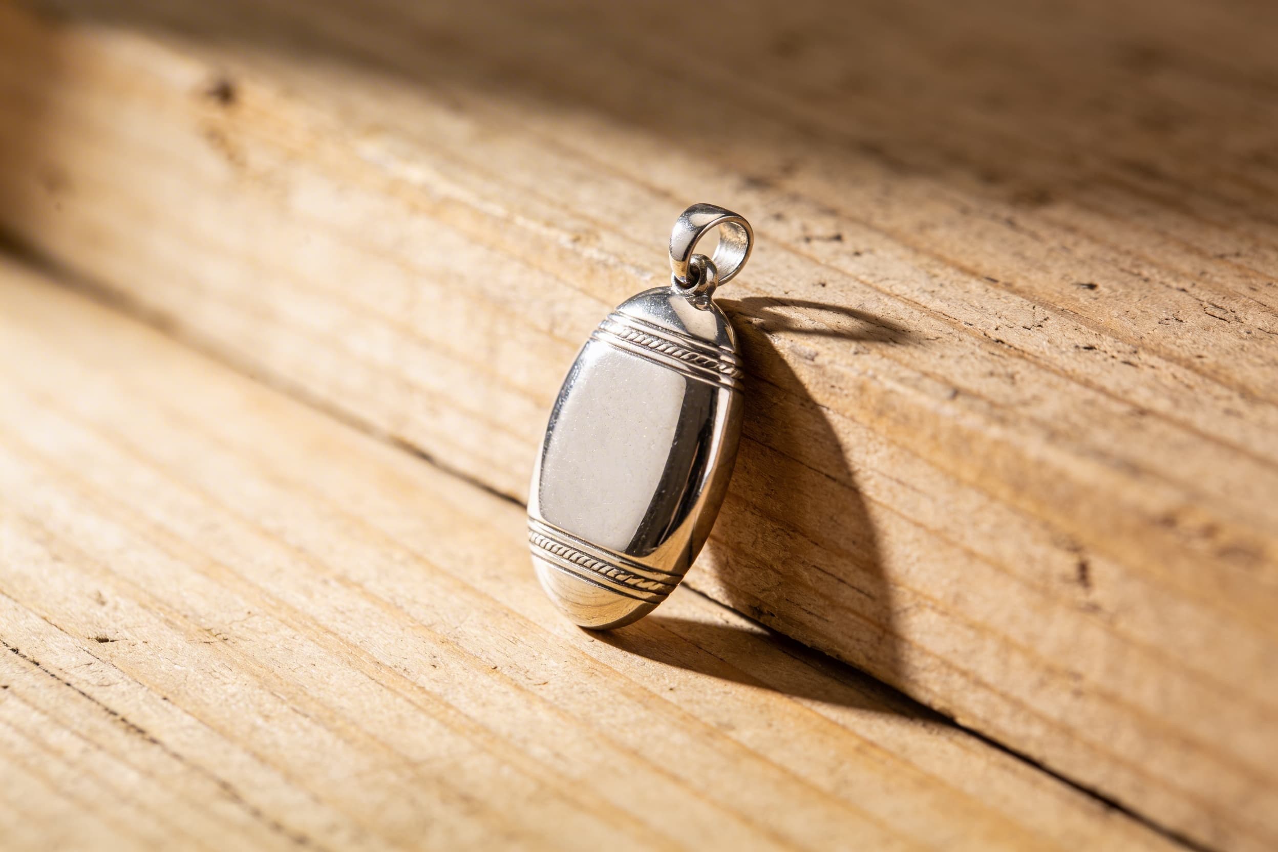 Engraved sterling silver cremation pendant with a name inscription shown in detail on a wooden surface