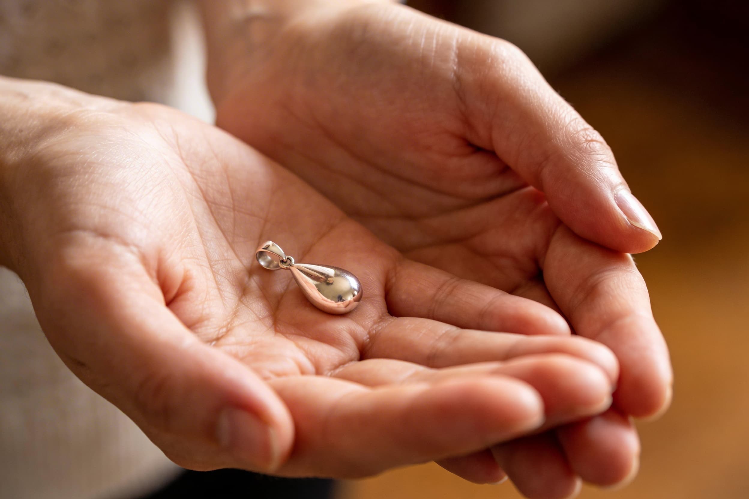 A delicate sterling silver teardrop cremation pendant resting in an open palm, soft natural light and a shallow depth of field background