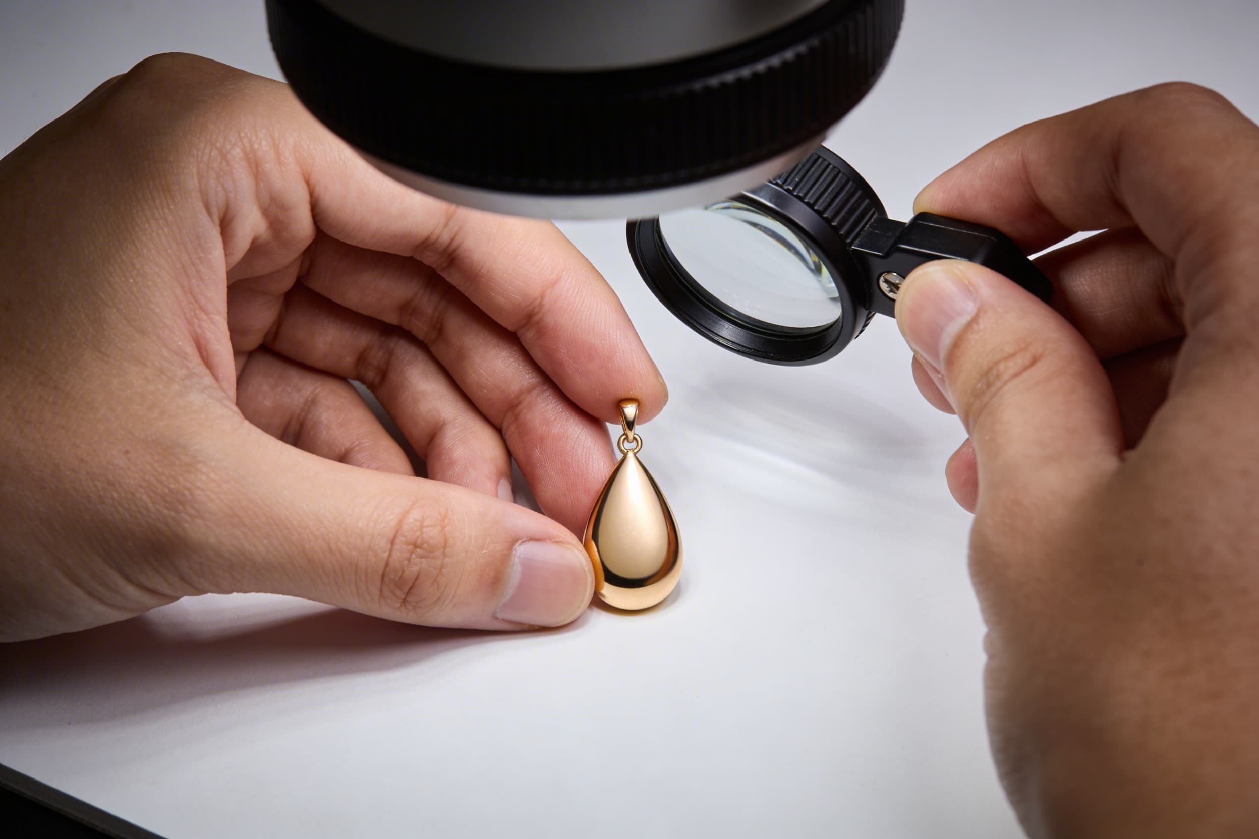 Close-up of a jeweler's hands gently inspecting a small pendant closure under a magnifying glass, soft studio lighting