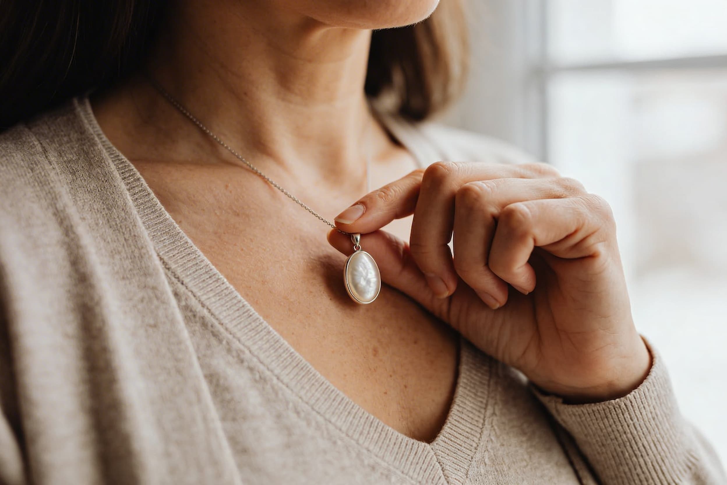 A woman holds a cremation necklace pendant in her hand around her neck