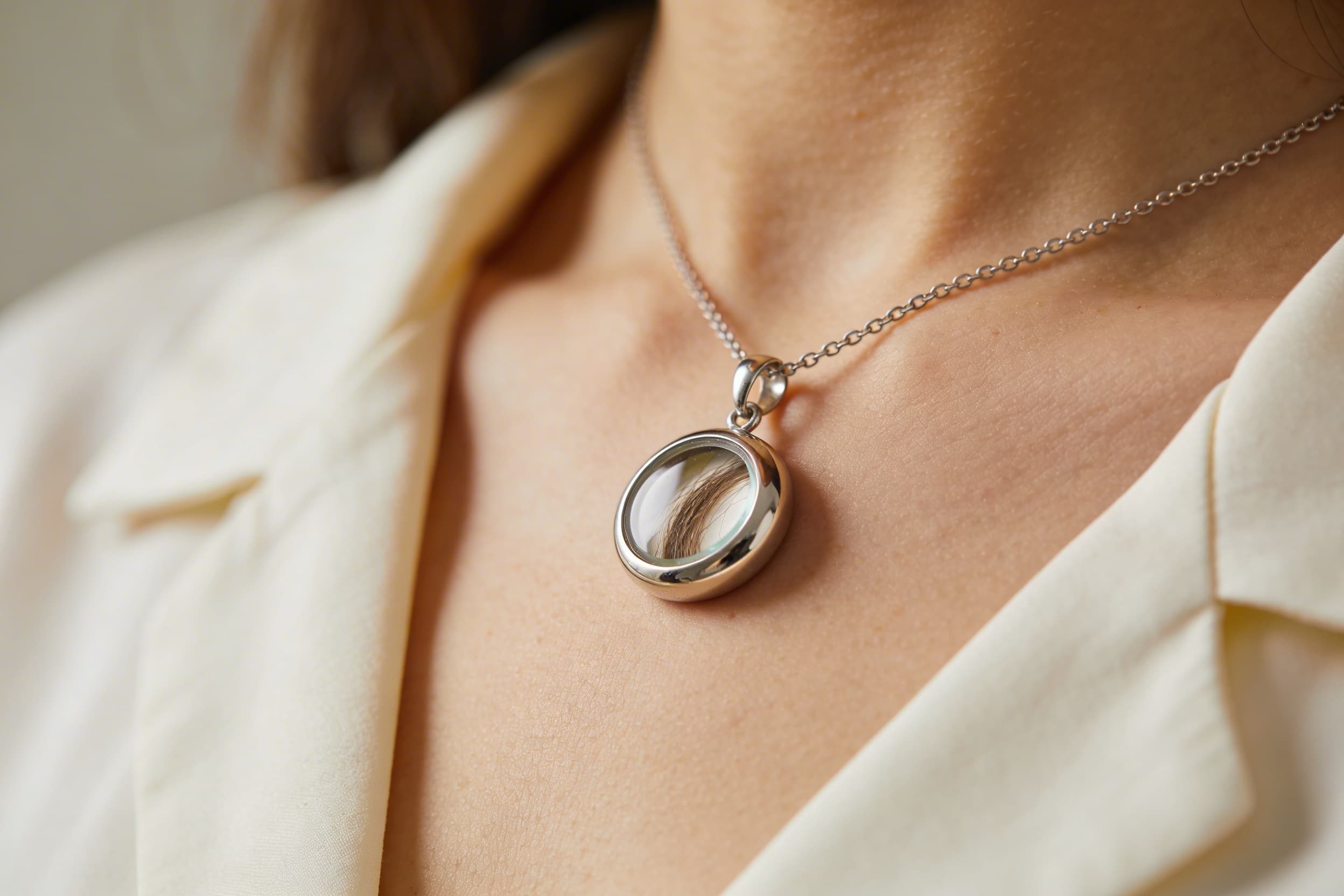 A delicate silver hair keepsake necklace pendant worn close to the heart, representing wearable lock of hair memorial jewelry