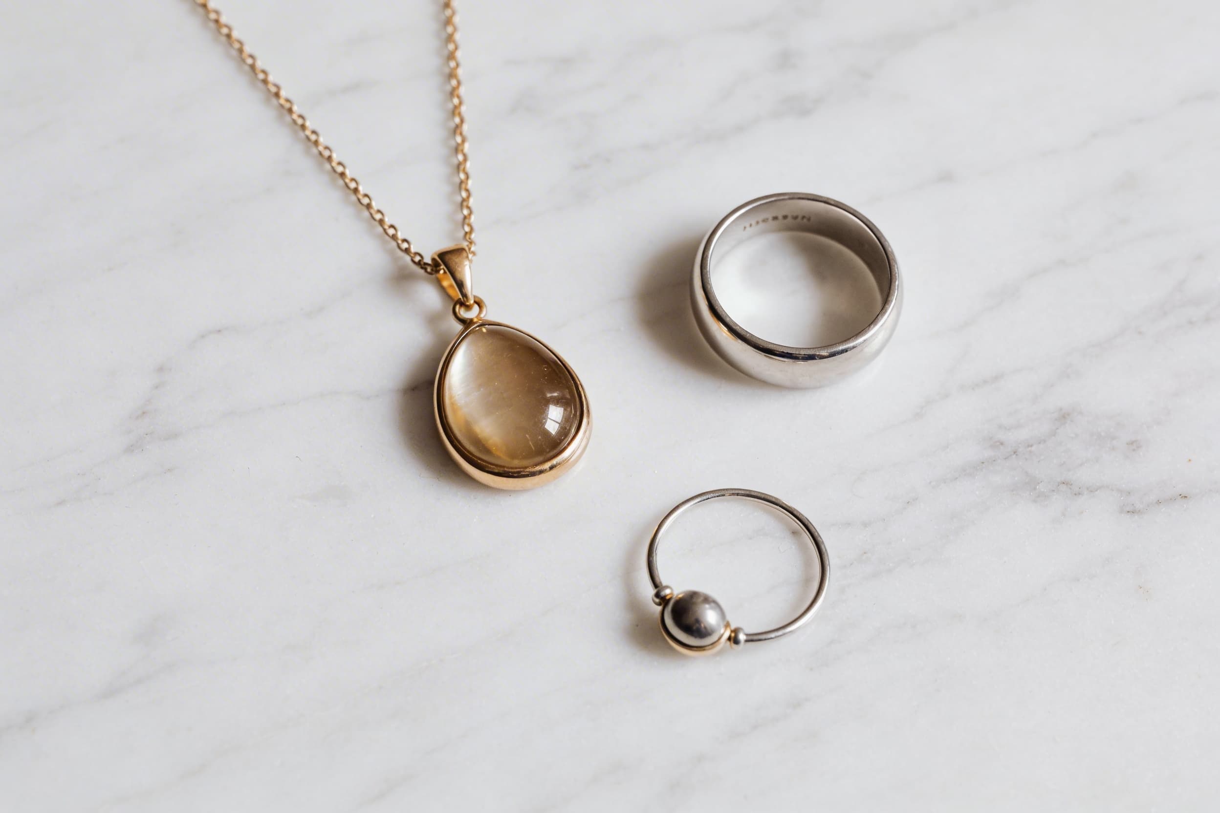A collection of modern memorial cremation jewelry pieces including a pendant, ring, and bracelet arranged on white marble