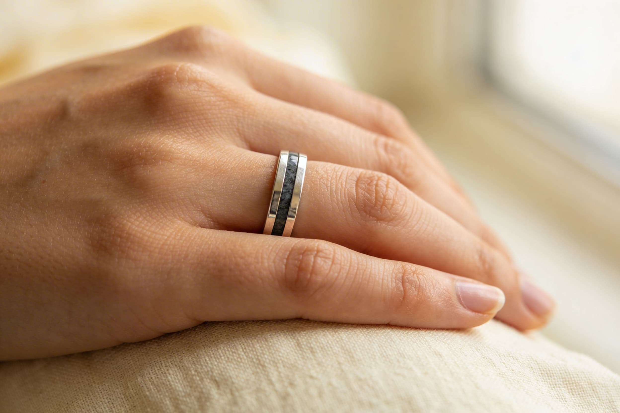 A close-up of a person's hand showing a simple sterling silver cremation ring with a subtle inlay design on the ring finger