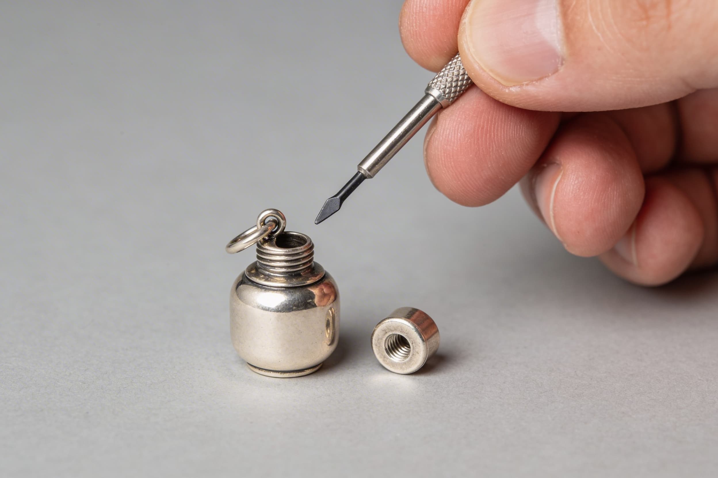 A small pet keepsake urn pendant with its screw-top cap removed next to a small screwdriver