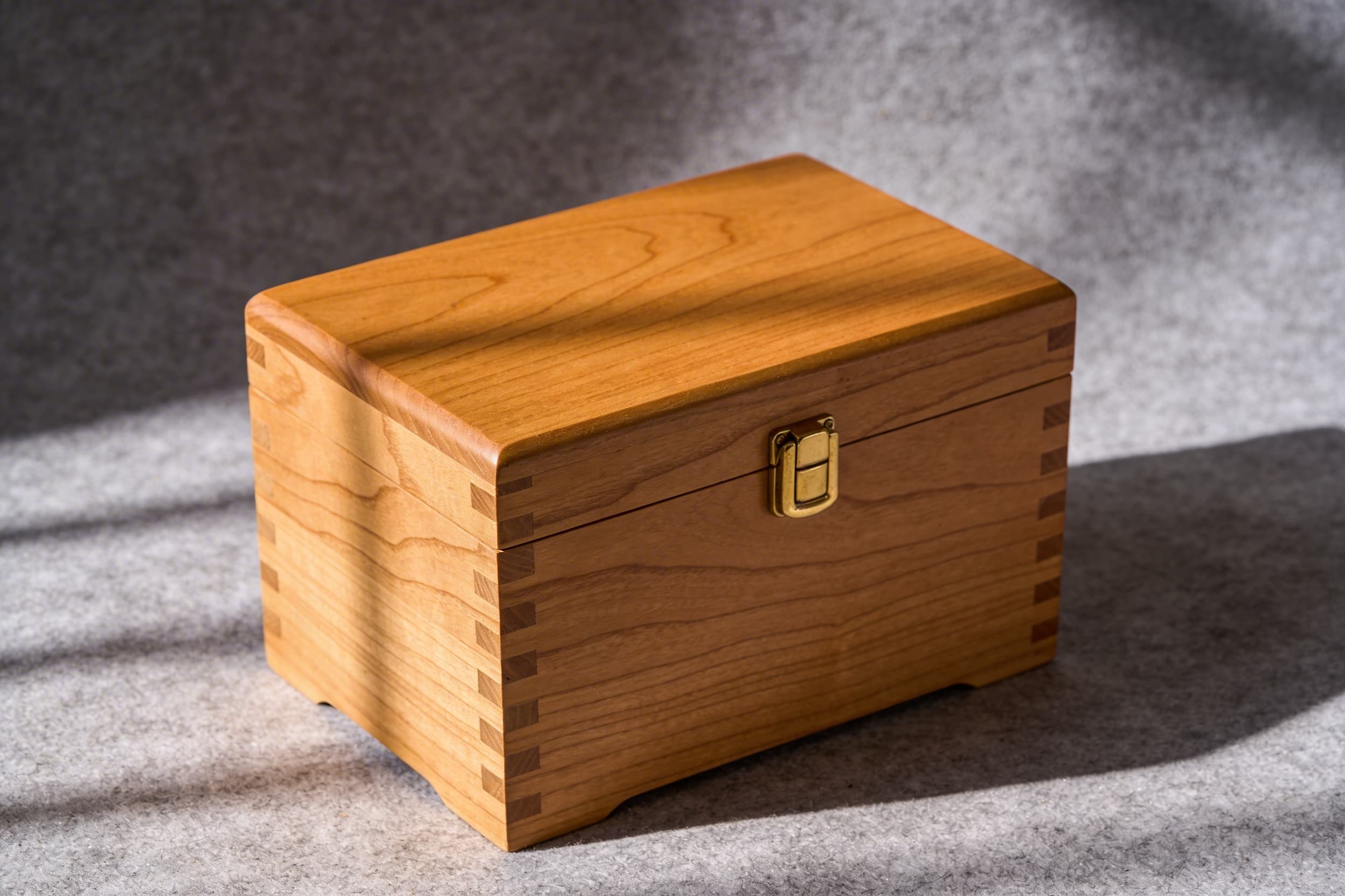 A handcrafted wooden pet urn with beautiful wood grain pattern and honey oak finish on gray felt