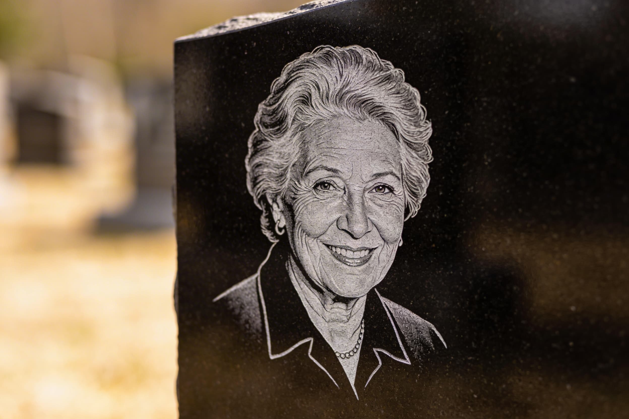 Close-up view of a laser-etched portrait on a polished black granite headstone showing detailed grayscale rendering of a person's face