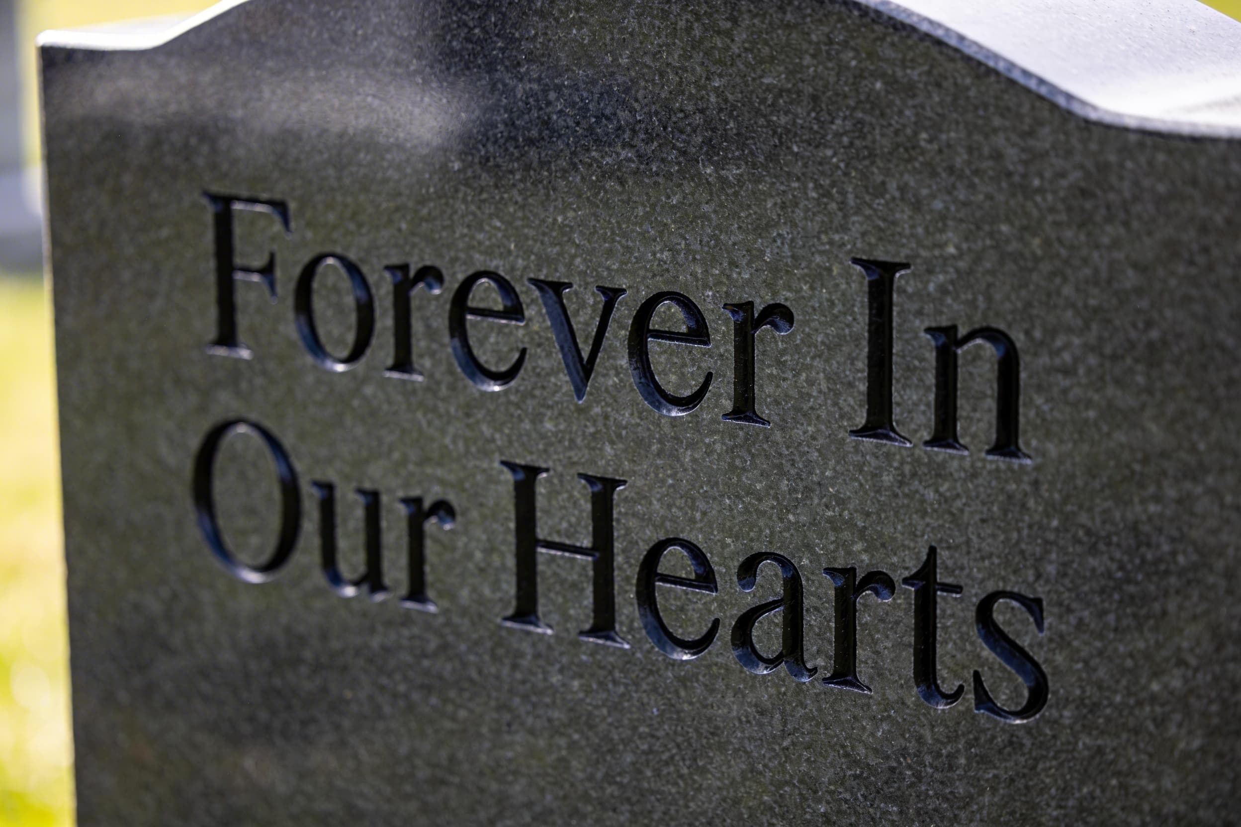 Close-up of a granite headstone with freshly restored black-painted inscriptions showing clear, readable lettering against polished stone