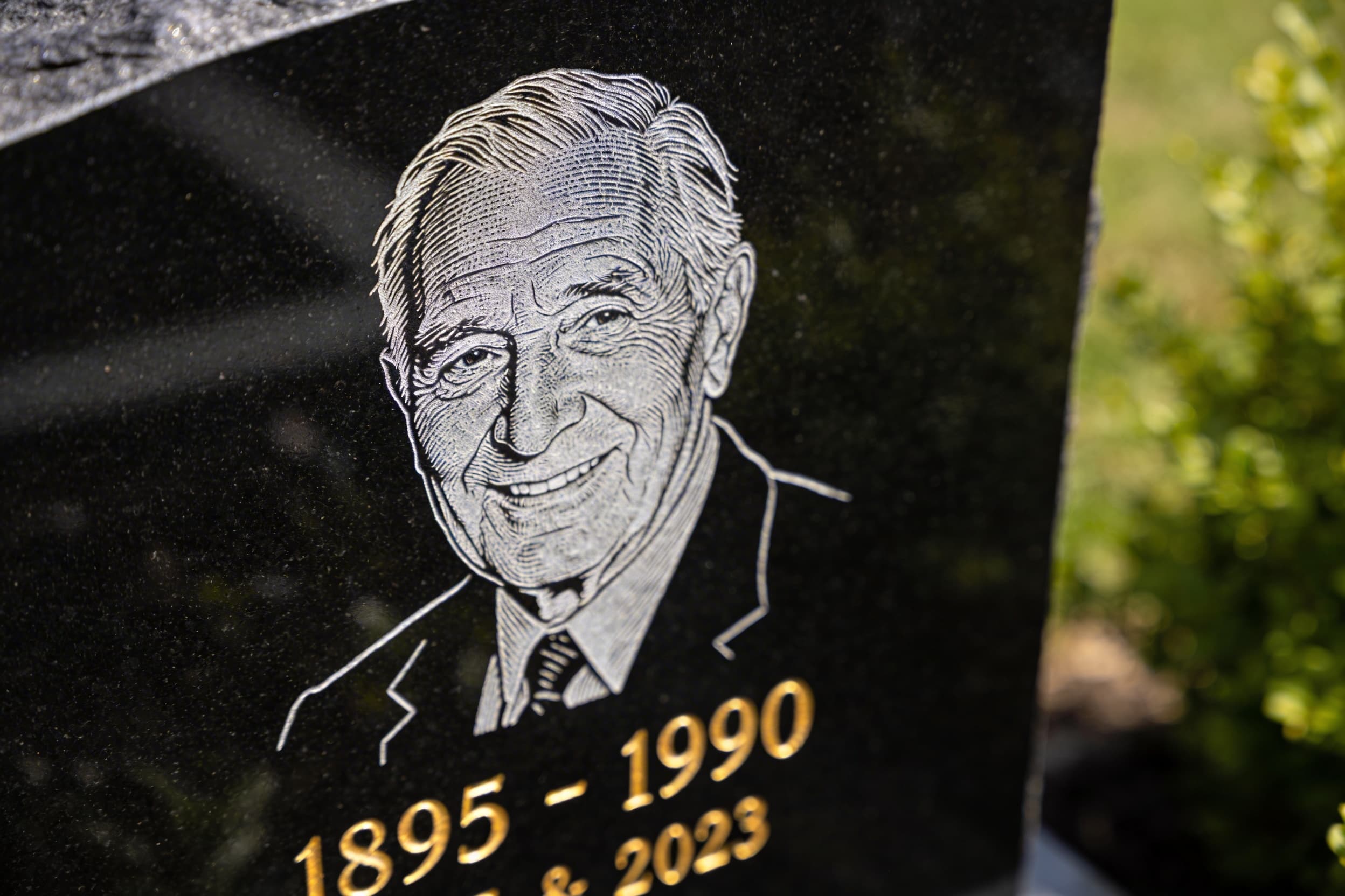 A close-up of a polished black granite headstone showing a laser-etched portrait next to sandblasted name and dates