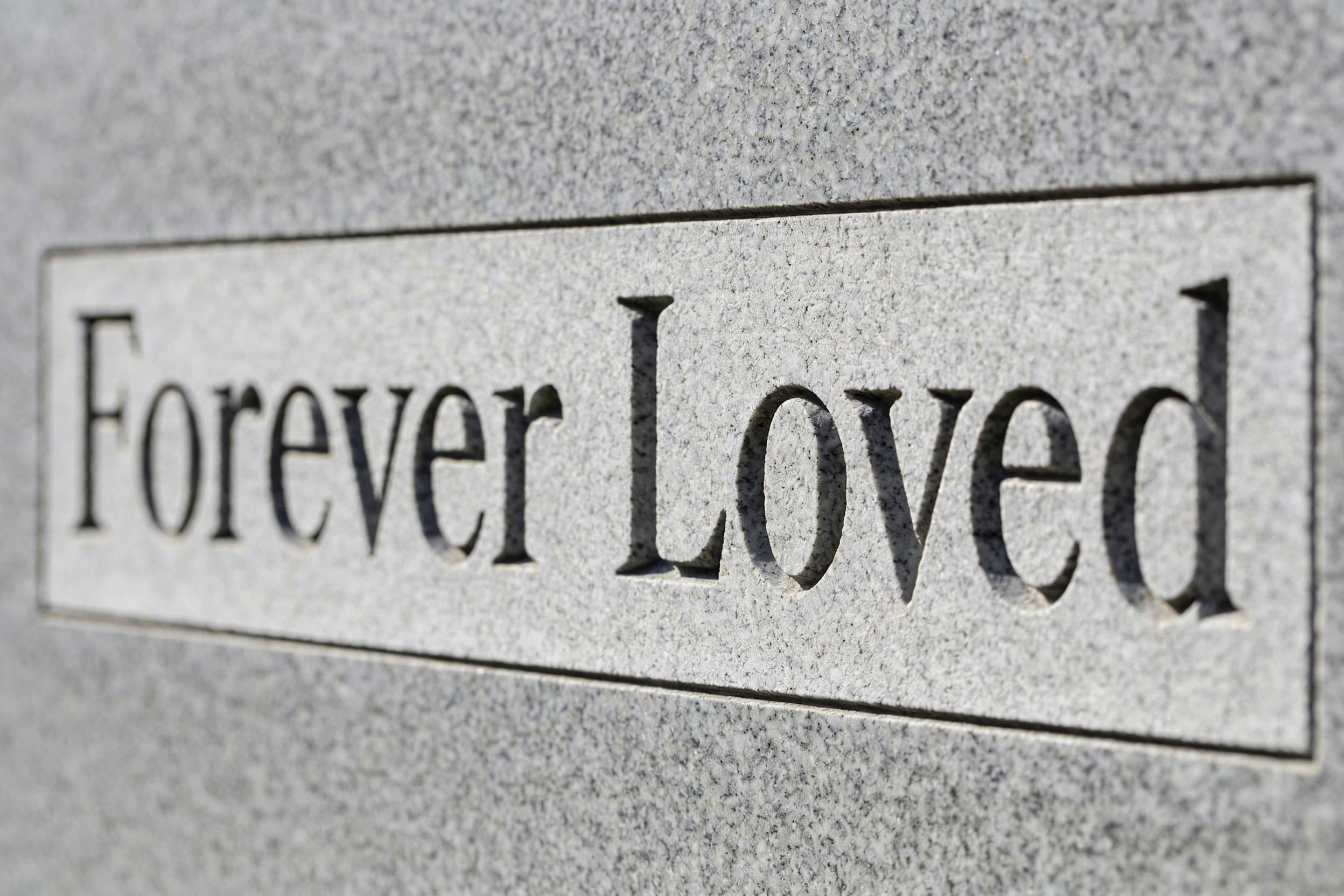 Close-up of deeply carved serif lettering on a light gray granite headstone showing crisp V-sunk letters