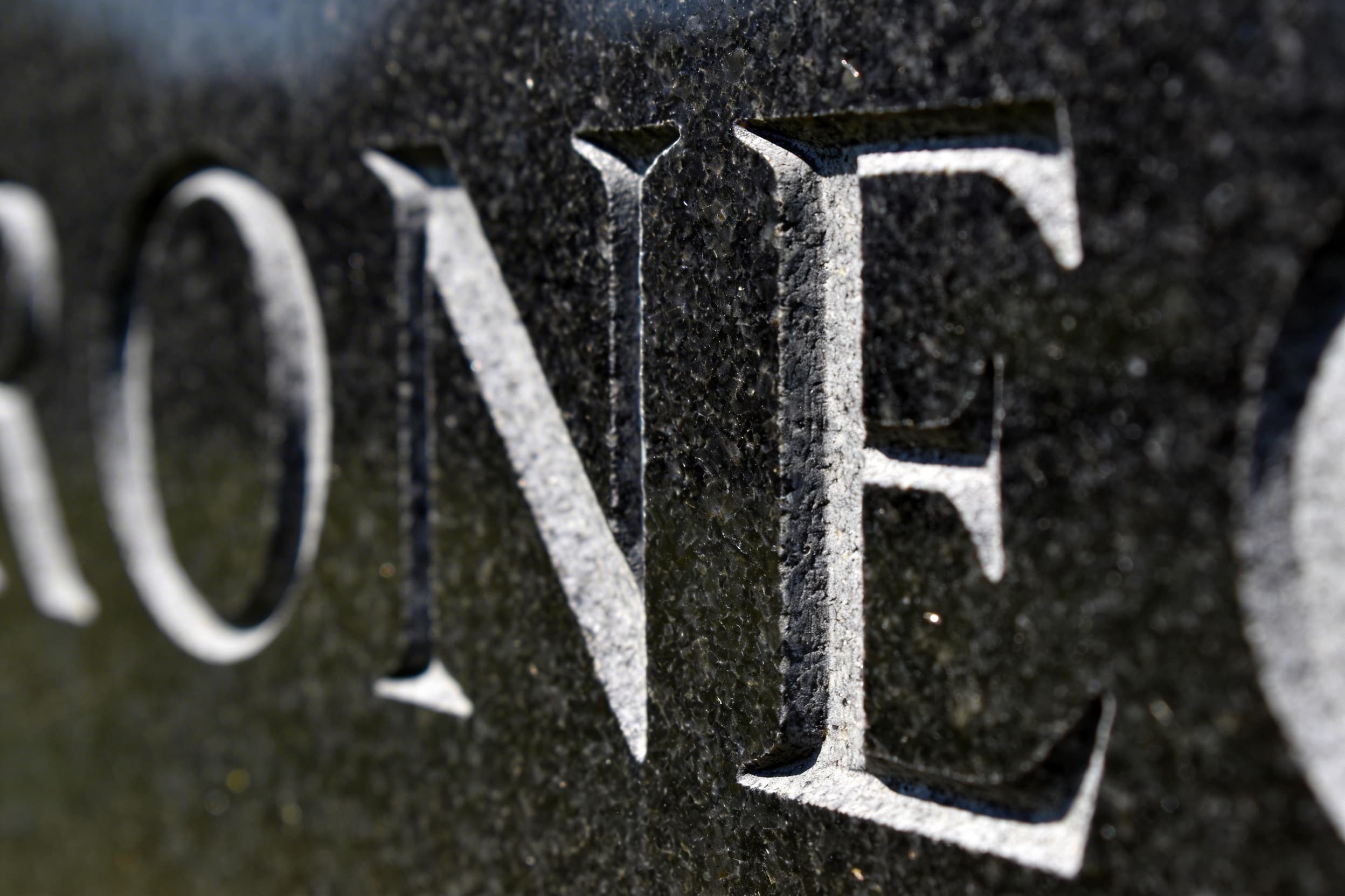 A close-up view of engraved serif lettering on a dark granite headstone surface showing crisp clean carved letters with soft natural light