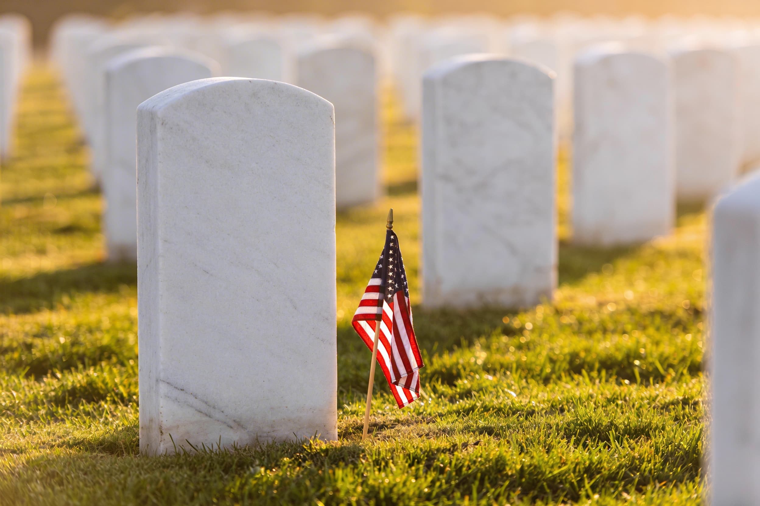 A government headstone at a national cemetery with a small American flag placed at its base