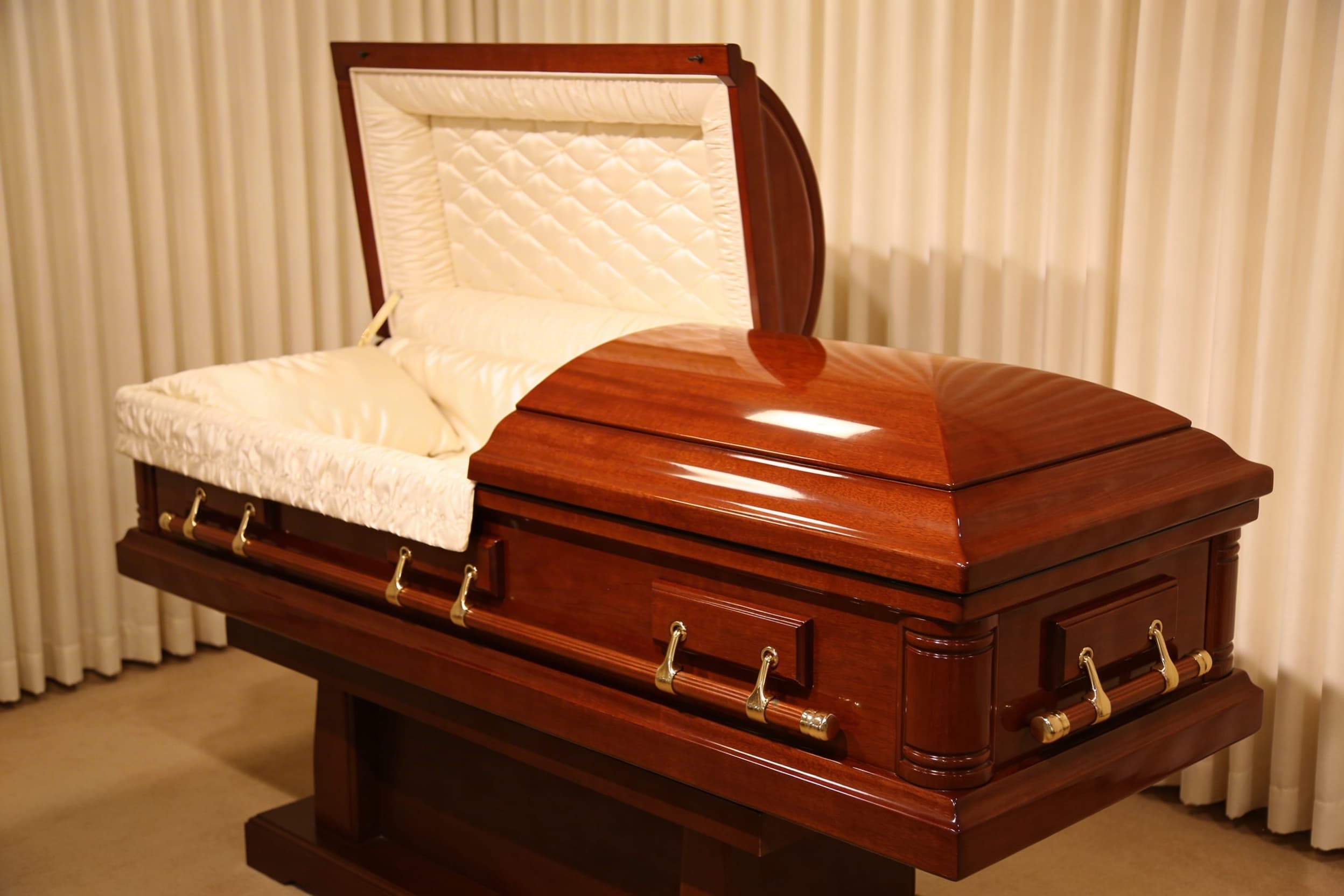 A polished hardwood casket with brass handles displayed in a softly lit funeral home showroom