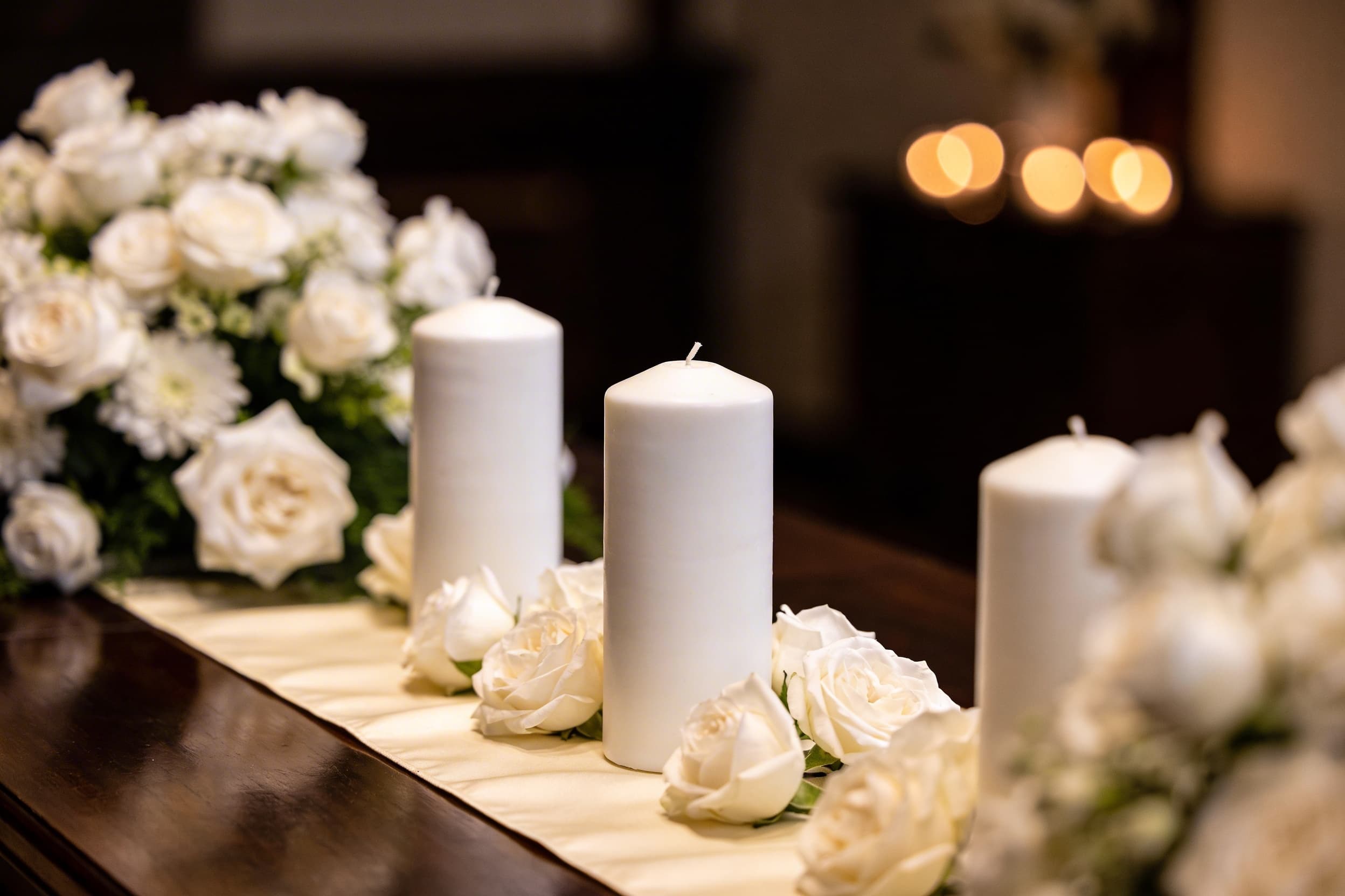 An elegant memorial service table arrangement with white candles and flowers in a warm, softly lit room