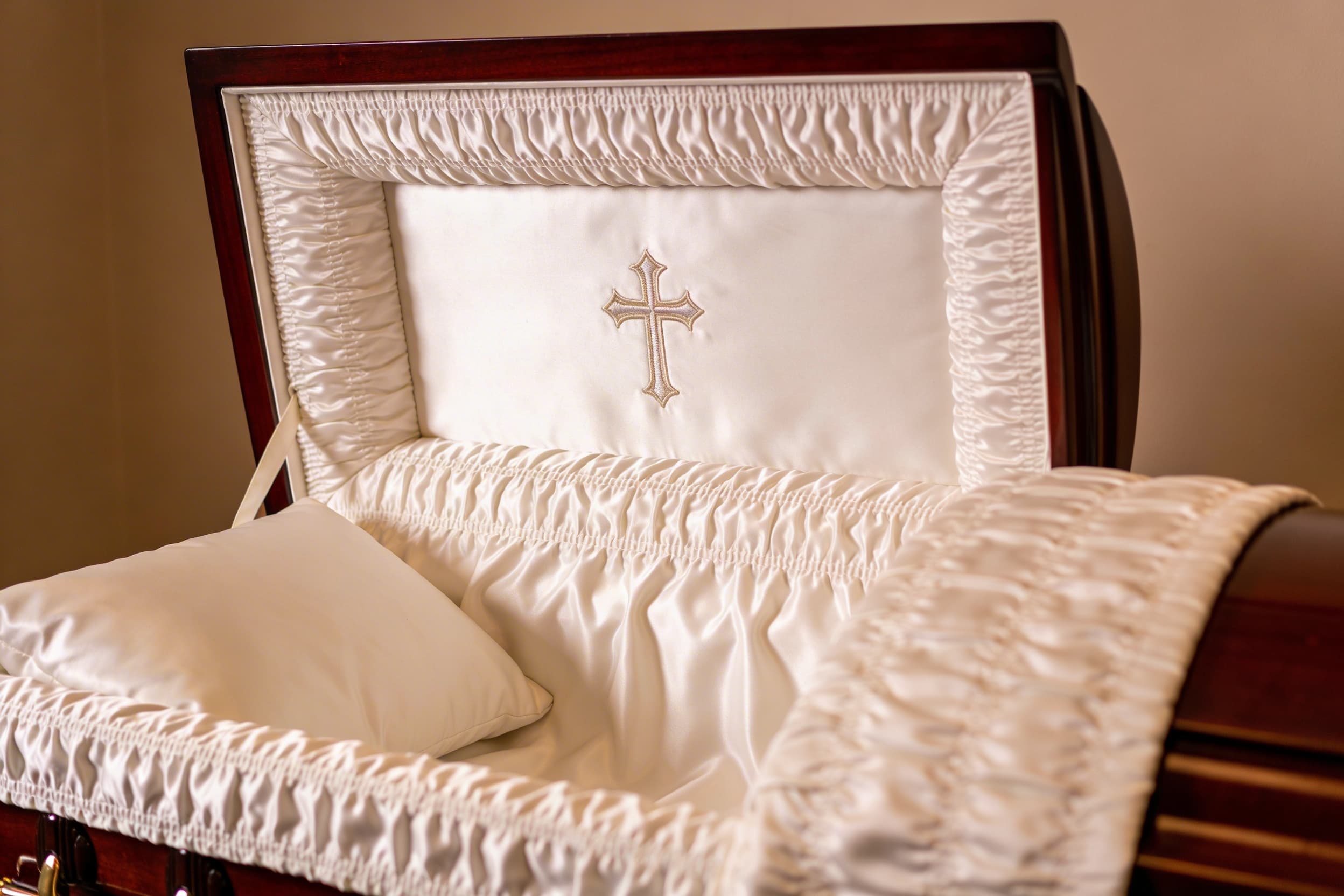 Close-up of a casket interior showing embroidered white satin lining with a cross design on the head panel