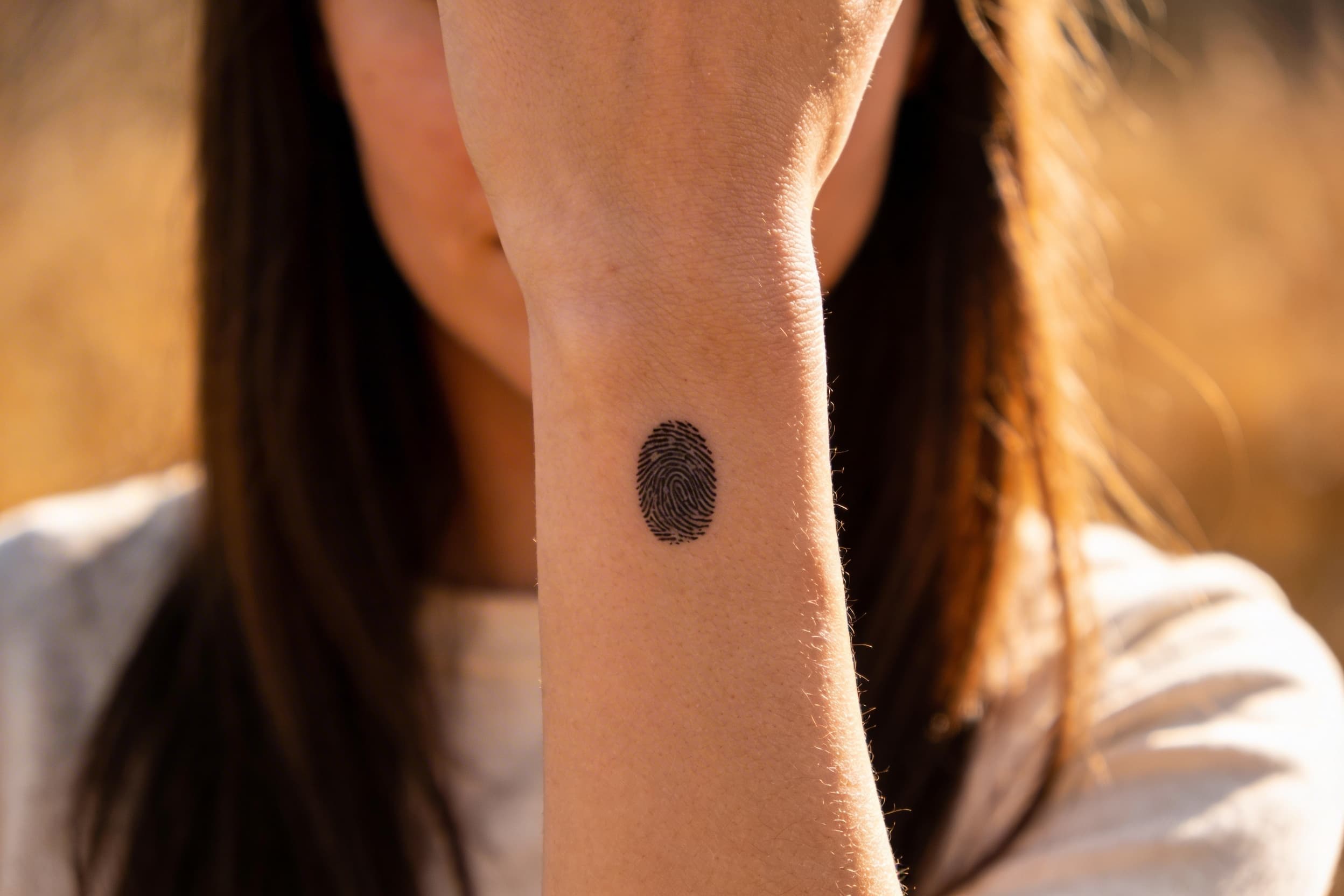 A close-up of a woman's inner wrist showing a small delicate fingerprint tattoo in black ink with visible ridge lines