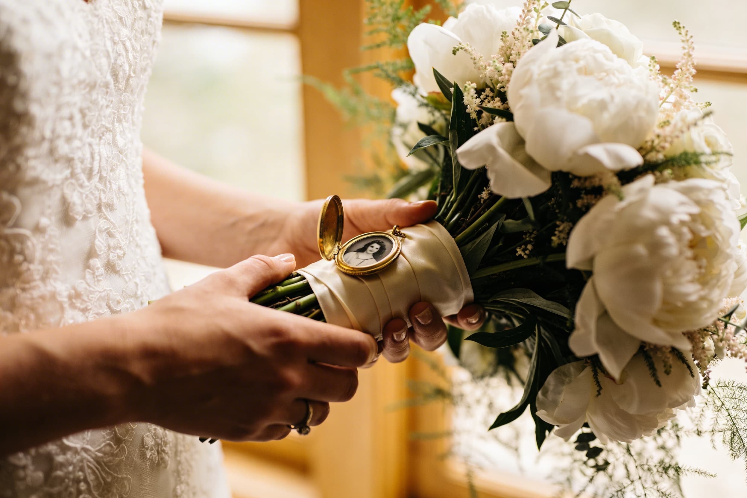 Close-up of a bridal bouquet wrapped in ivory ribbon with a small oval photo locket of a family member attached to the stems