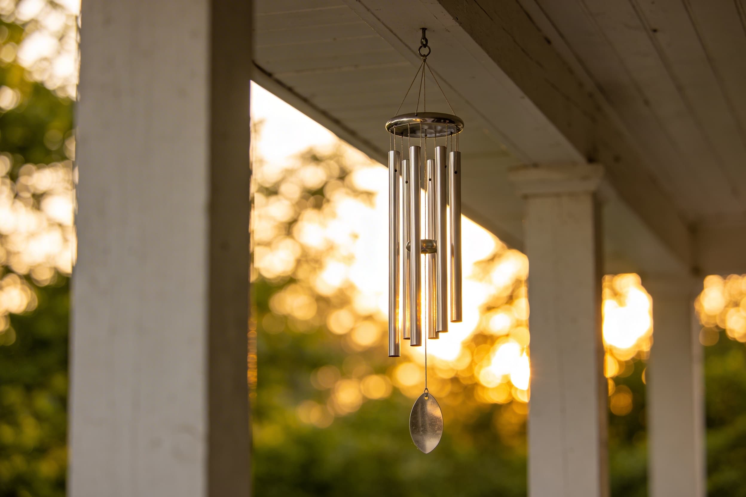 A personalized memorial wind chime hanging from a porch beam at sunset with warm golden light