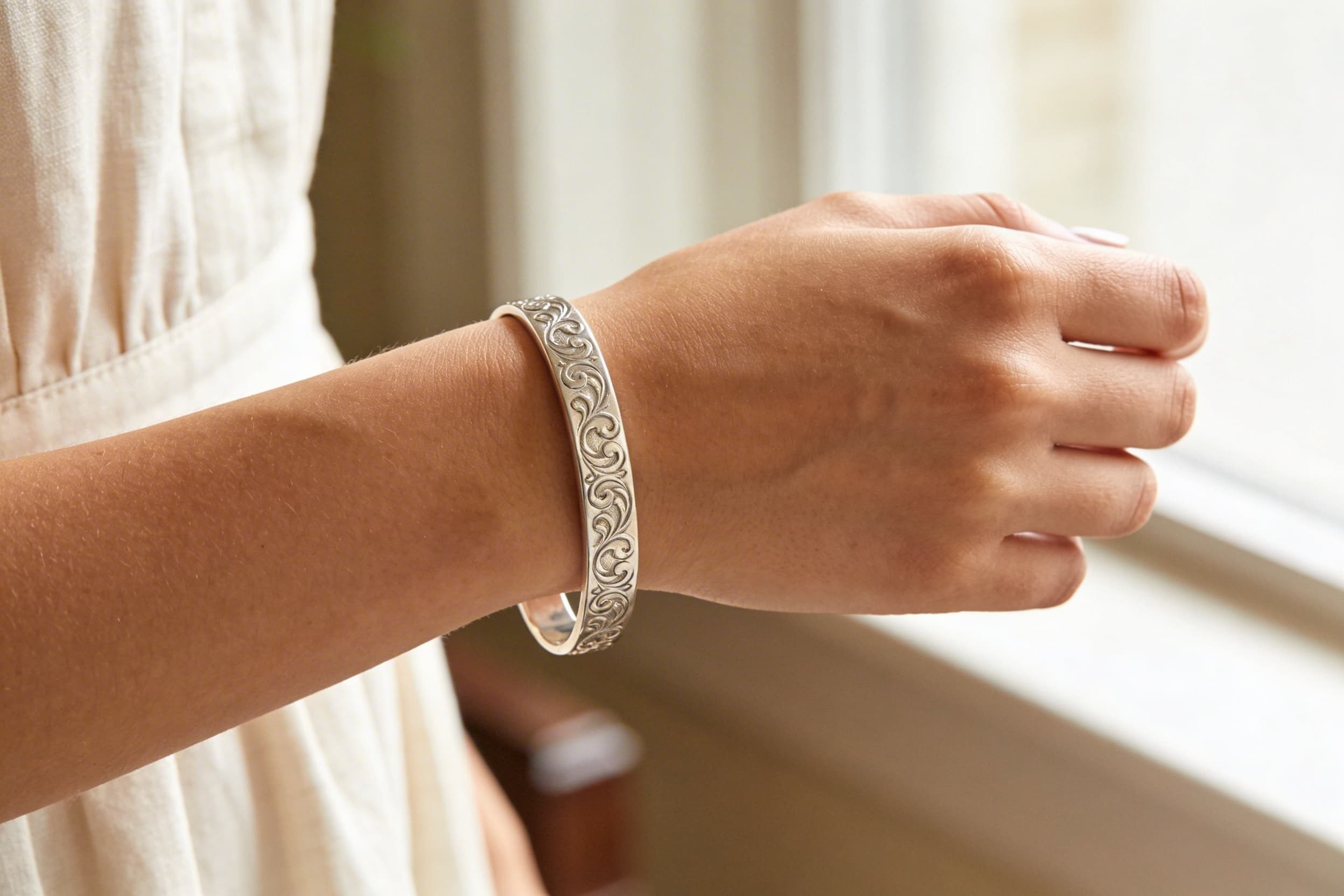 A sterling silver cremation bracelet worn on a wrist with soft natural light highlighting the engraved details