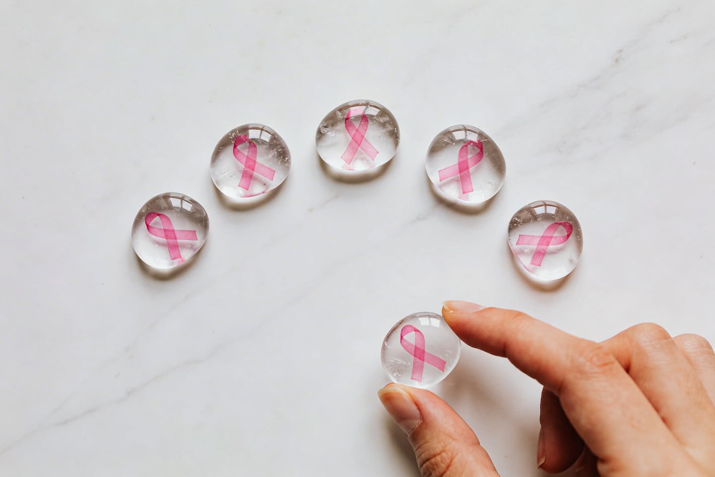 Five pink ribbon awareness stones arranged on a white marble surface with one being held gently between fingers