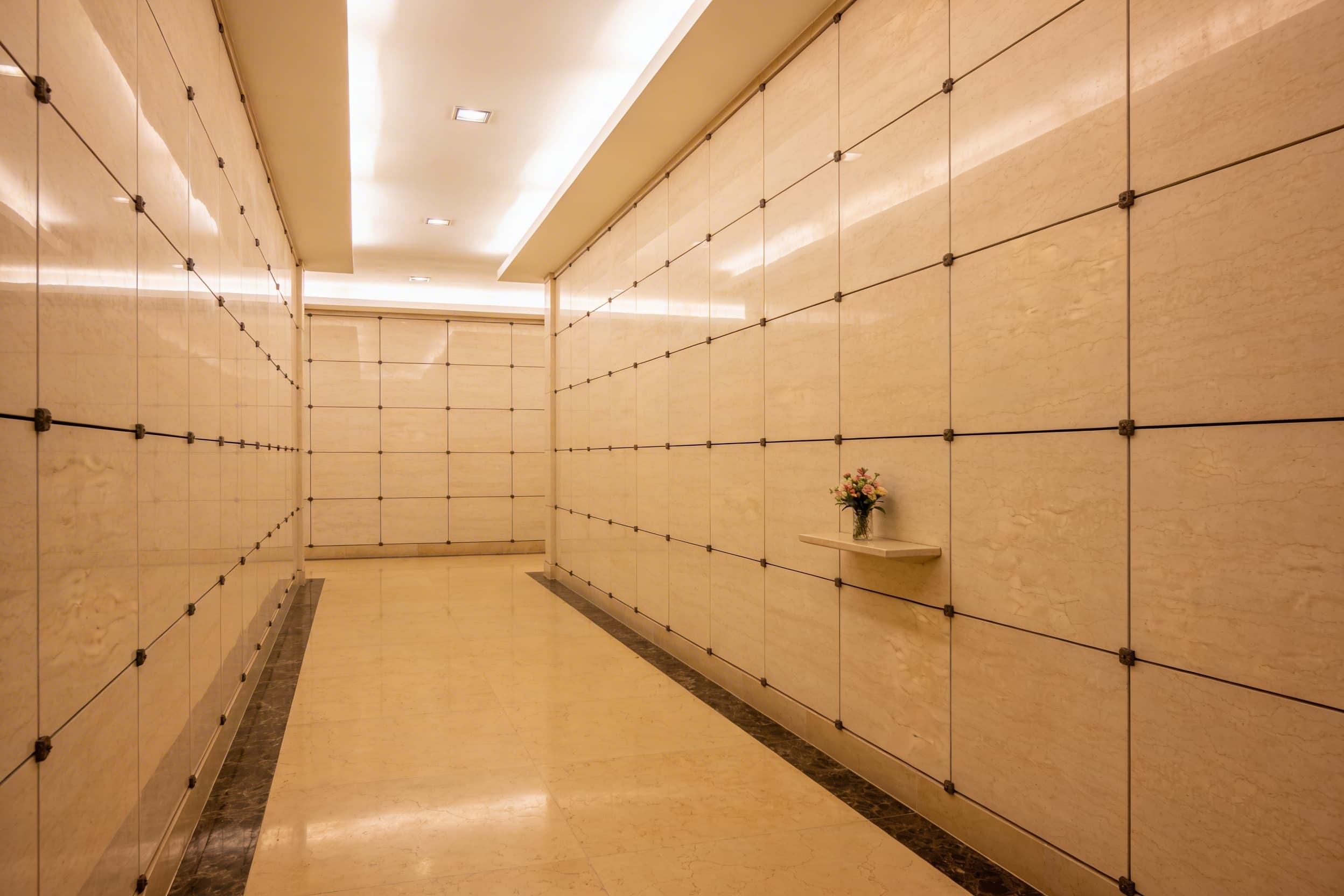 A serene indoor columbarium with rows of marble-front niches and soft overhead lighting in a quiet memorial chapel
