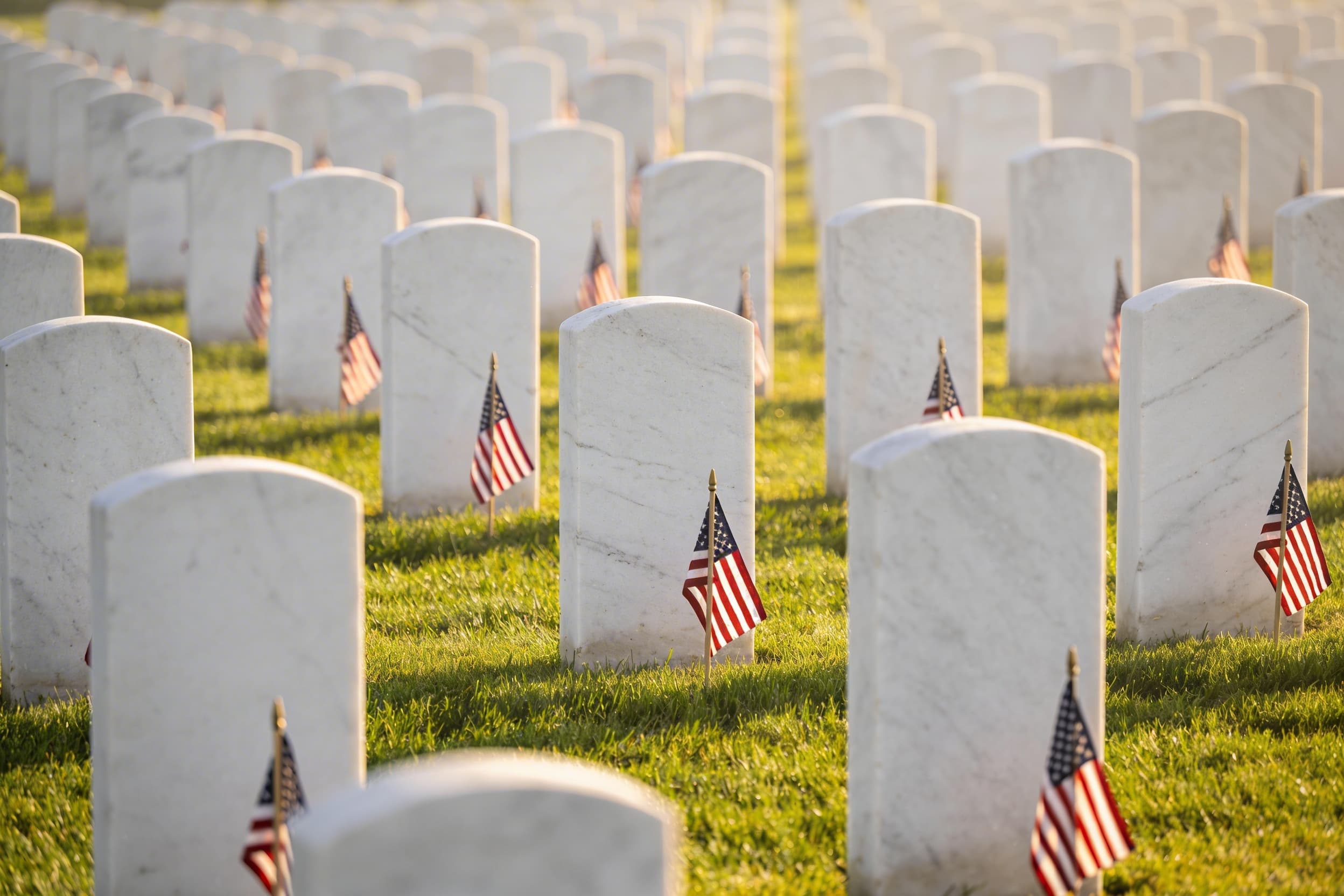 Rows of white government headstones in a VA national cemetery with American flags placed at each grave during a Memorial Day observance
