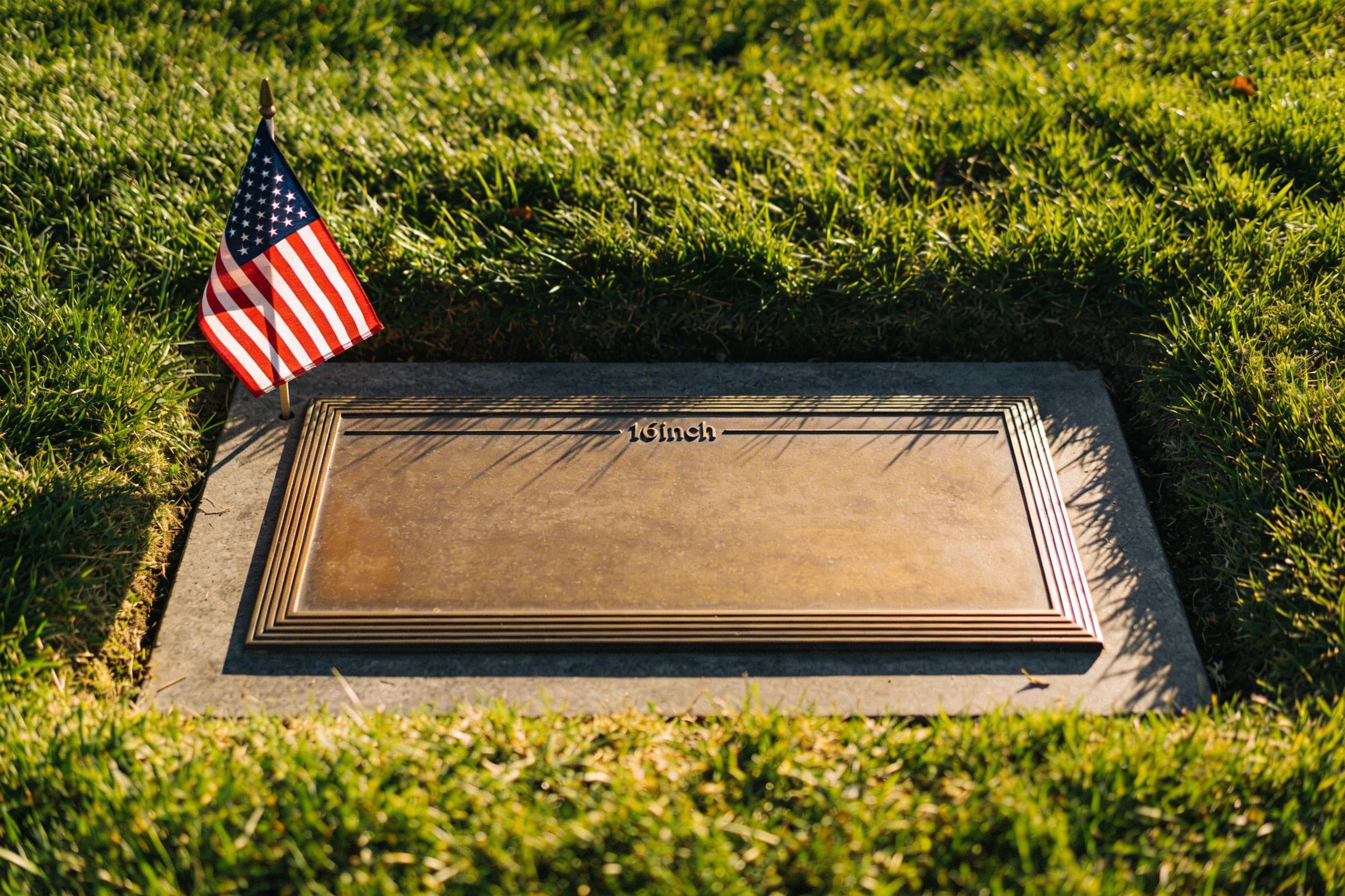 A bronze veteran grave marker set in green cemetery grass with a small American flag placed beside it