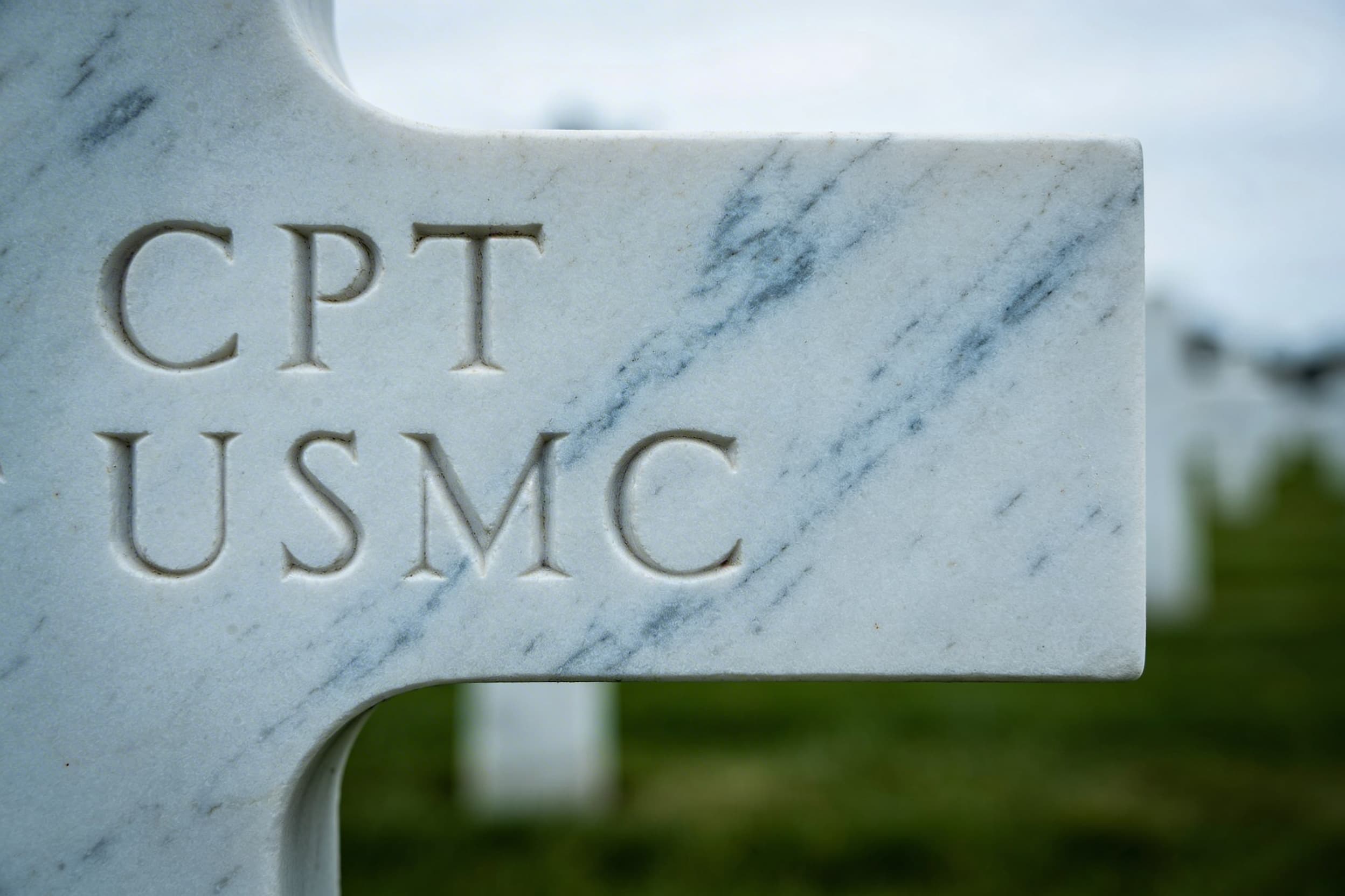 Close-up of a white marble military headstone showing inscribed rank abbreviation, branch of service, war service designation, and dates