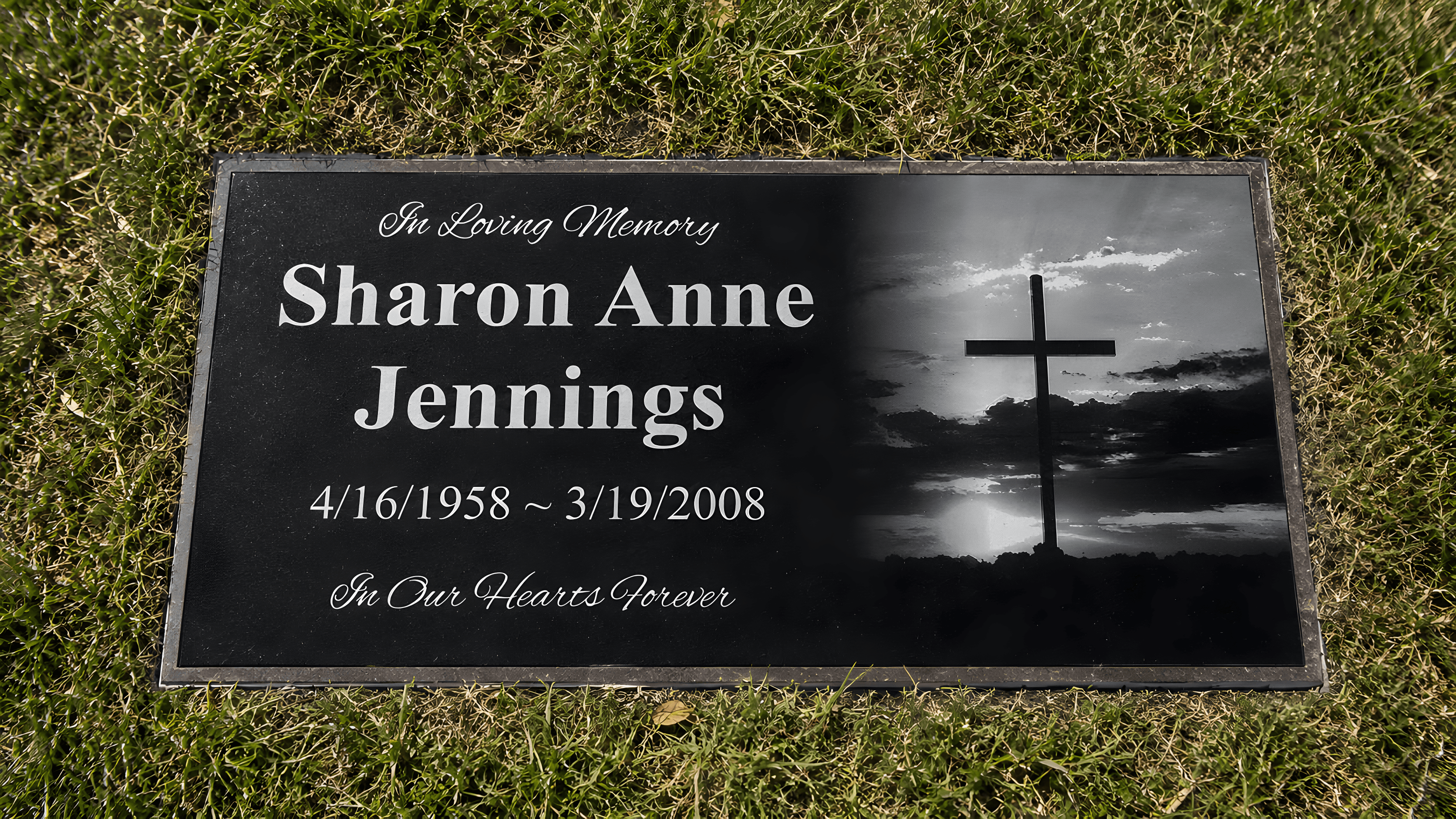 A black granite laser-etched grave marker in the cemetery green grass.