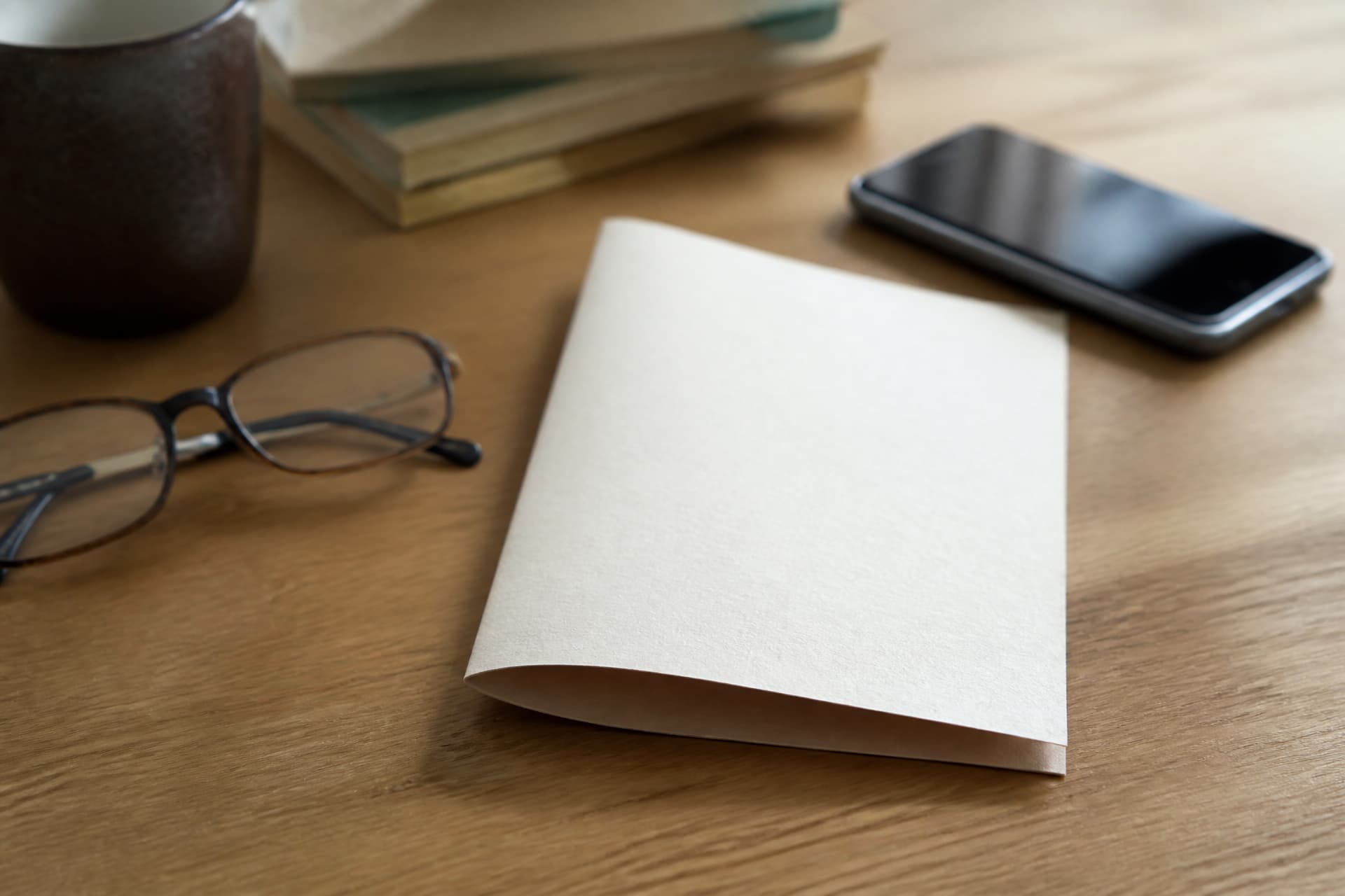 A printed sheet of paper folded once on a desk beside a phone and a pair of reading glasses, soft daylight