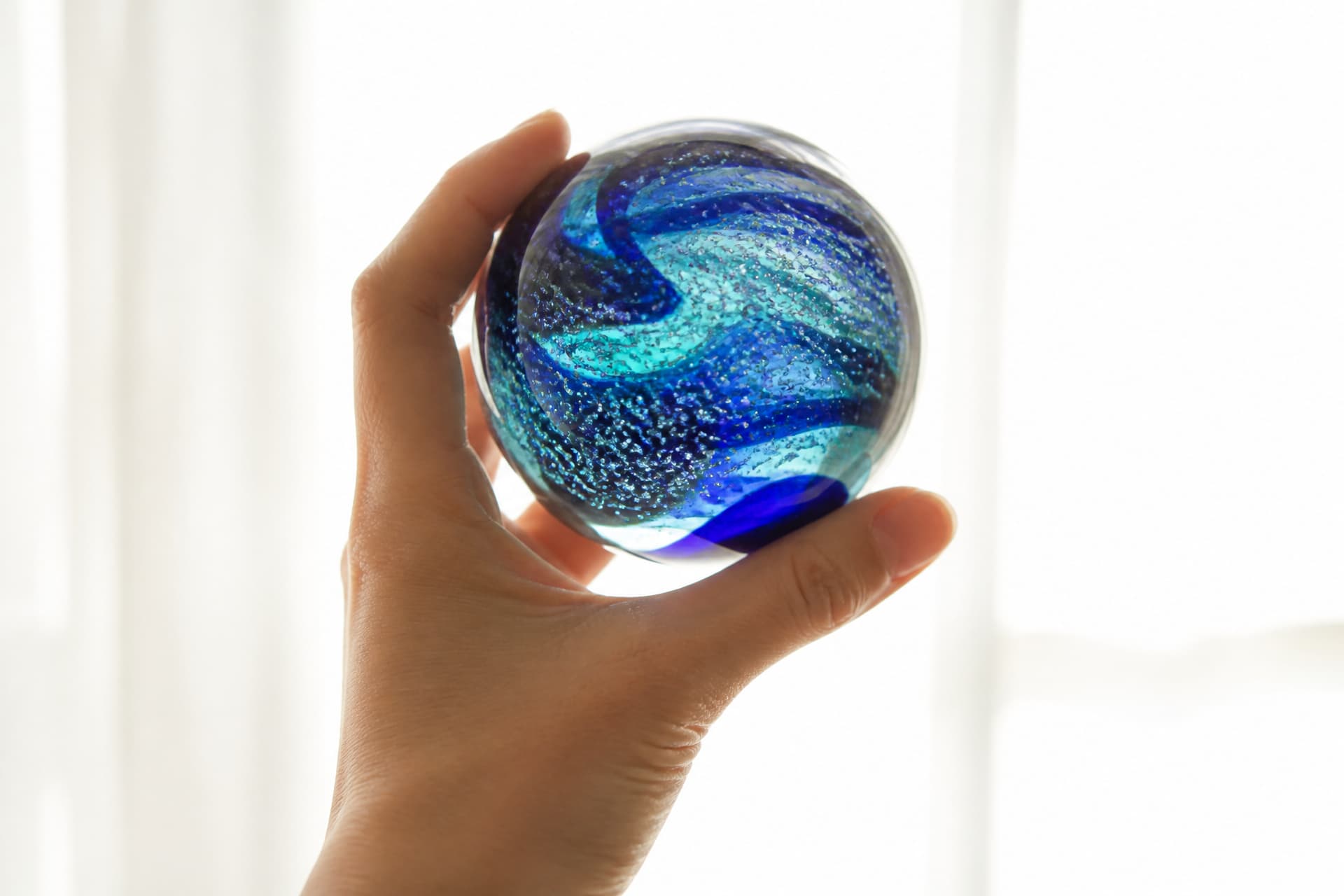 A hand-blown glass keepsake with swirling color held up to a window, light passing through the flecks suspended inside it
