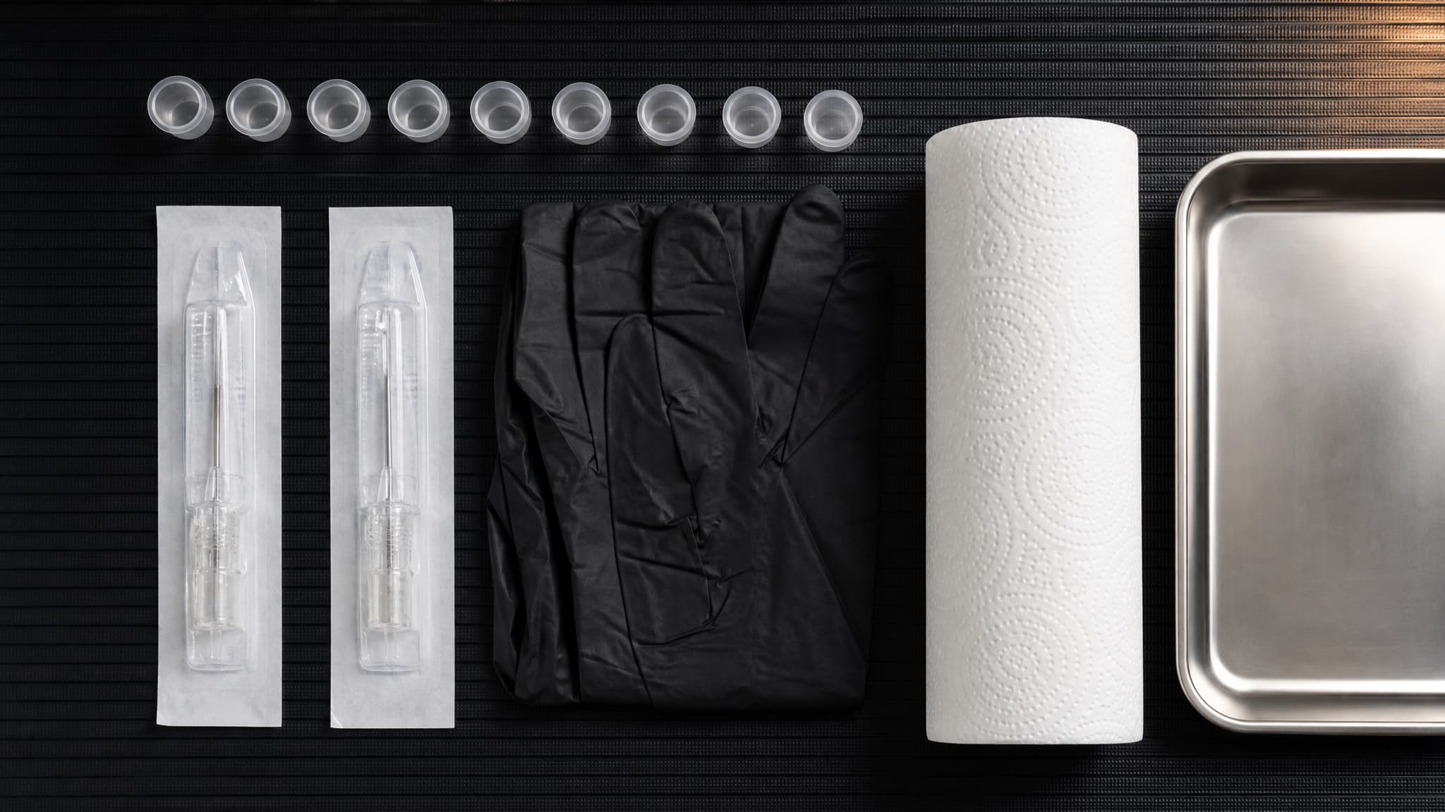 A tattoo artist's clean workstation with capped ink caps, sealed needle packets and gloves laid out on a black mat