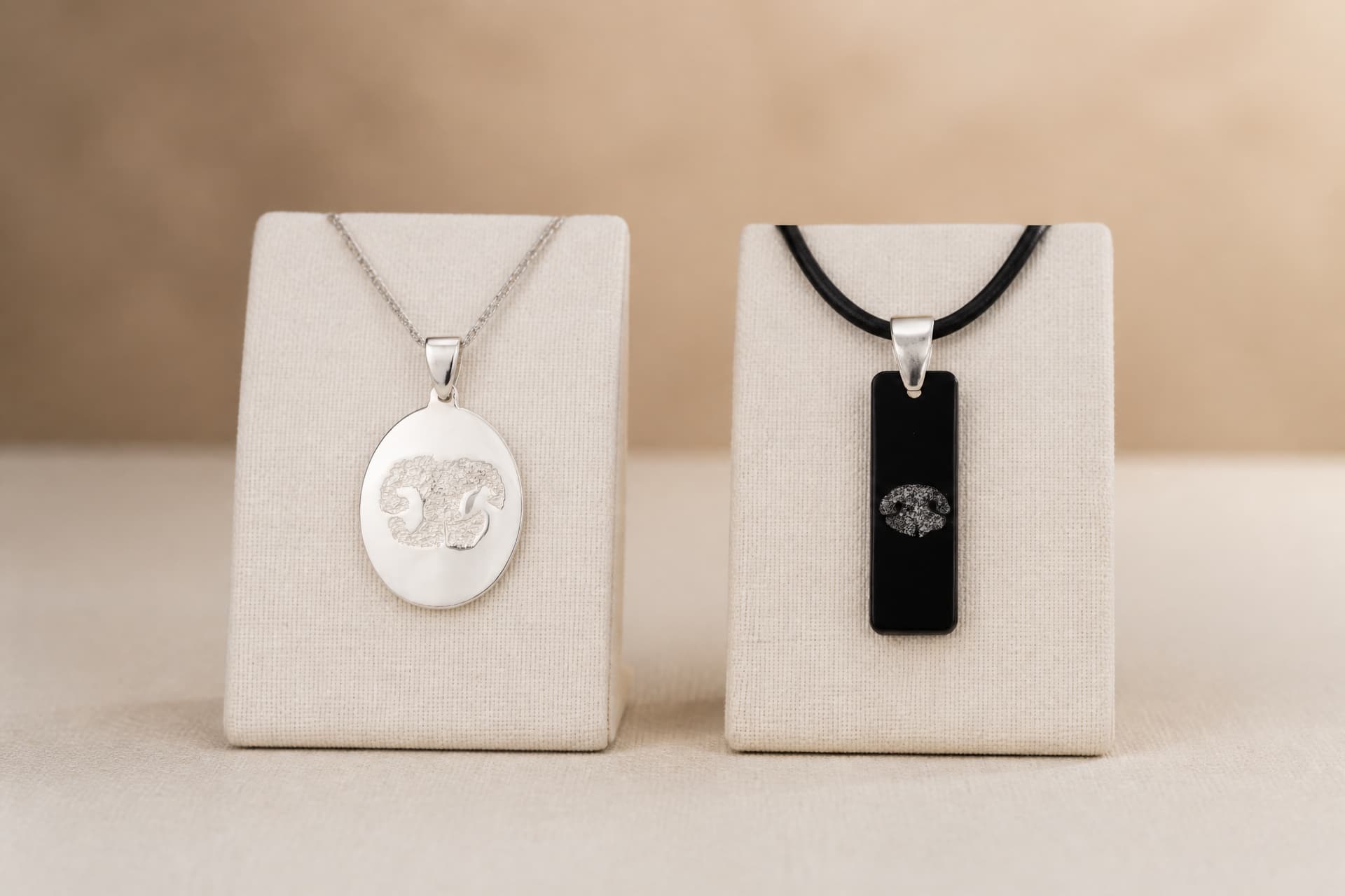 Two pet print pendants on cream display stands โ an oval sterling pendant with a raised nose print, and a black bar pendant with a nose print