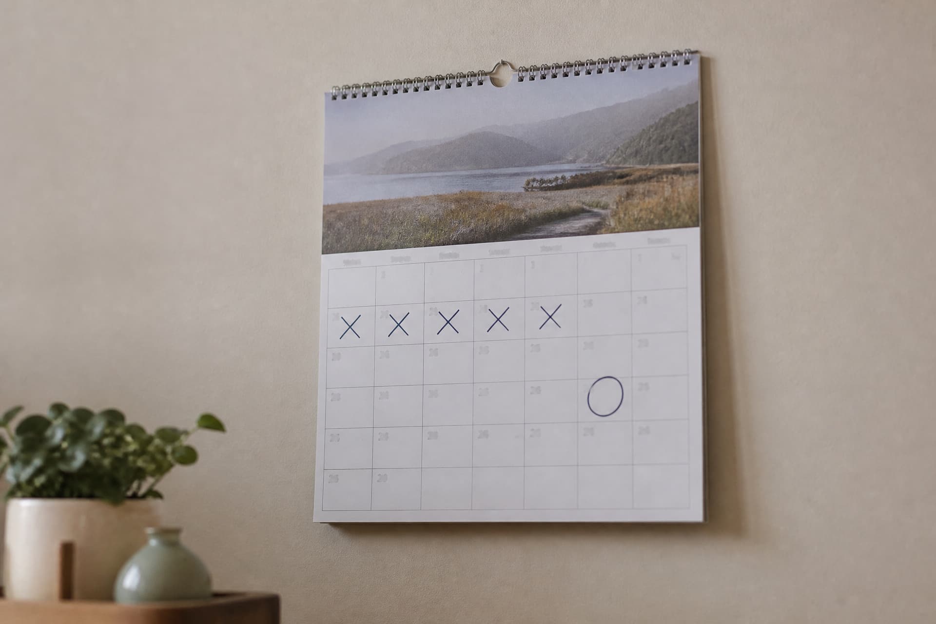 A wall calendar with several consecutive days marked in pen and a separate date circled weeks later, hanging on a plain wall