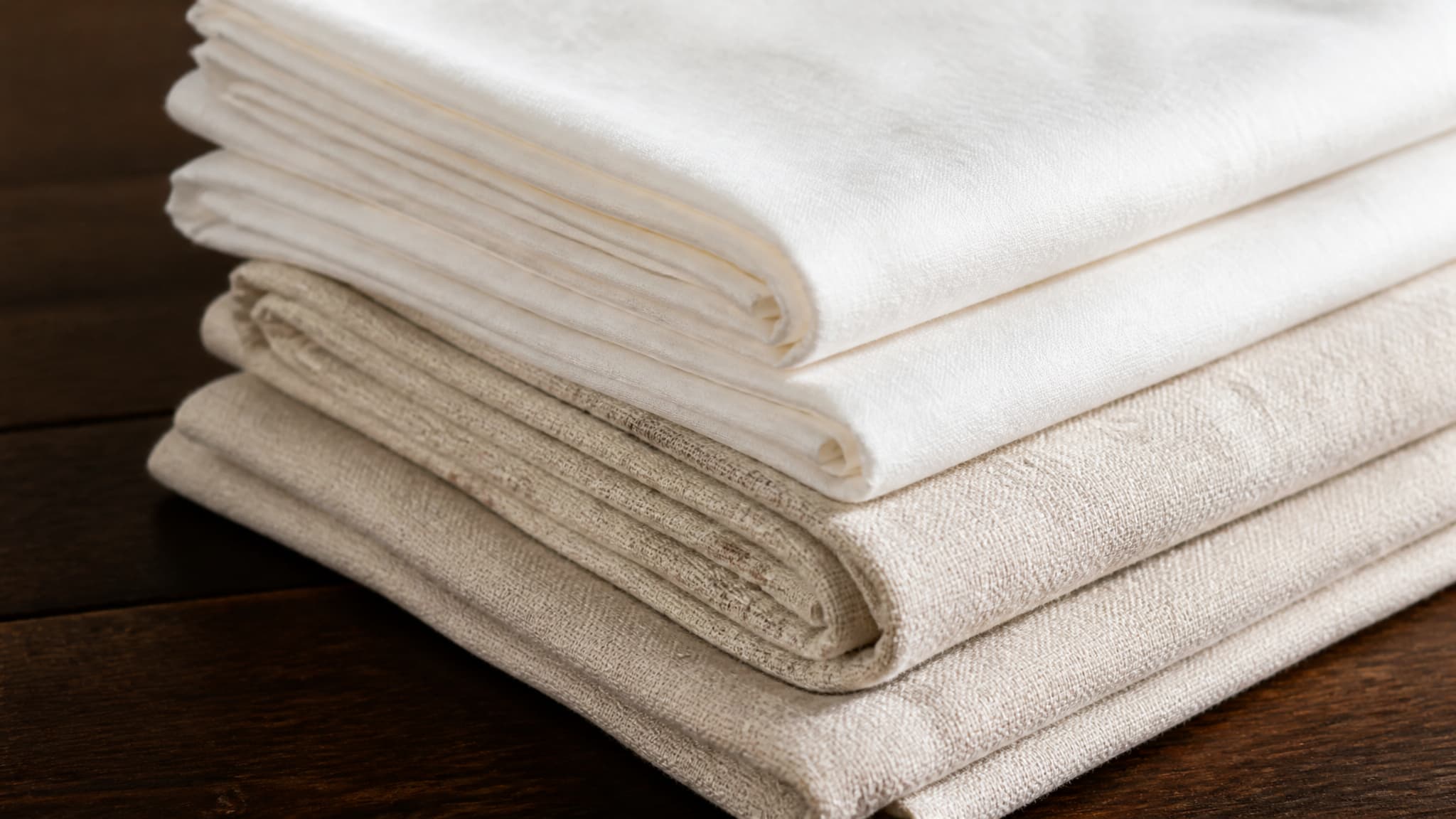 Folded lengths of plain white and undyed cloth resting on a dark wooden surface