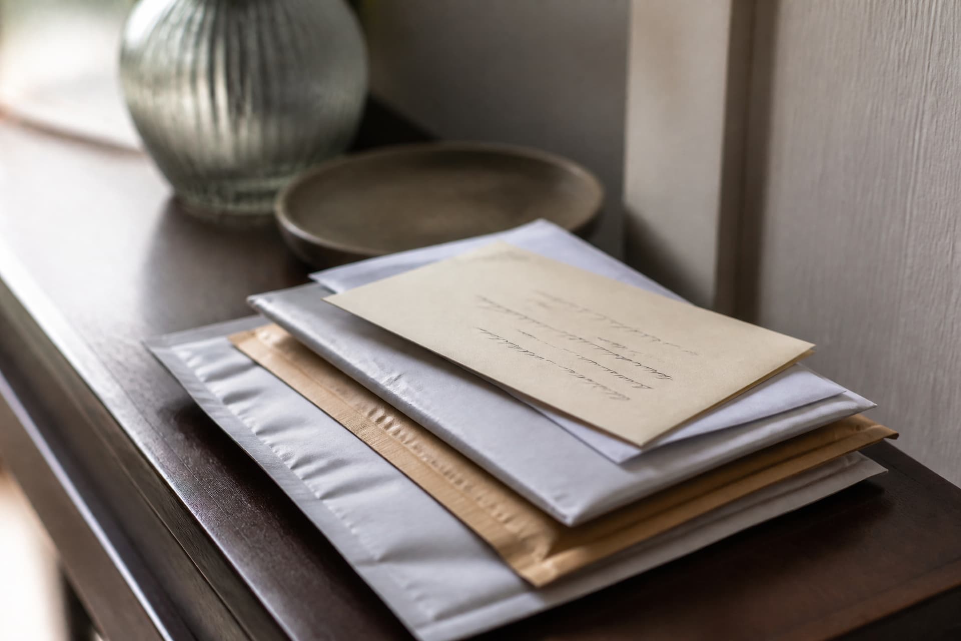 A small stack of unopened mail on a dark hall table with a cream hand-addressed envelope resting on top, the handwriting too soft to read