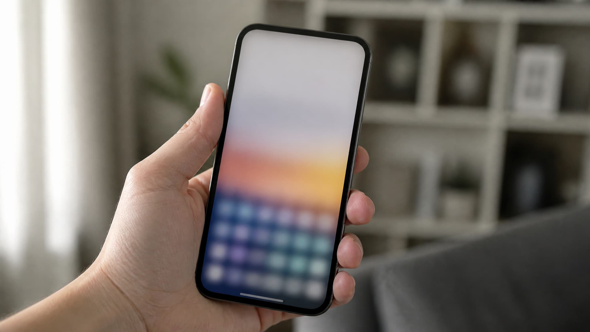 A phone held in one hand in soft daylight, the screen showing an open keyboard panel as a blurred grid of small colored squares, a living room out of focus behind