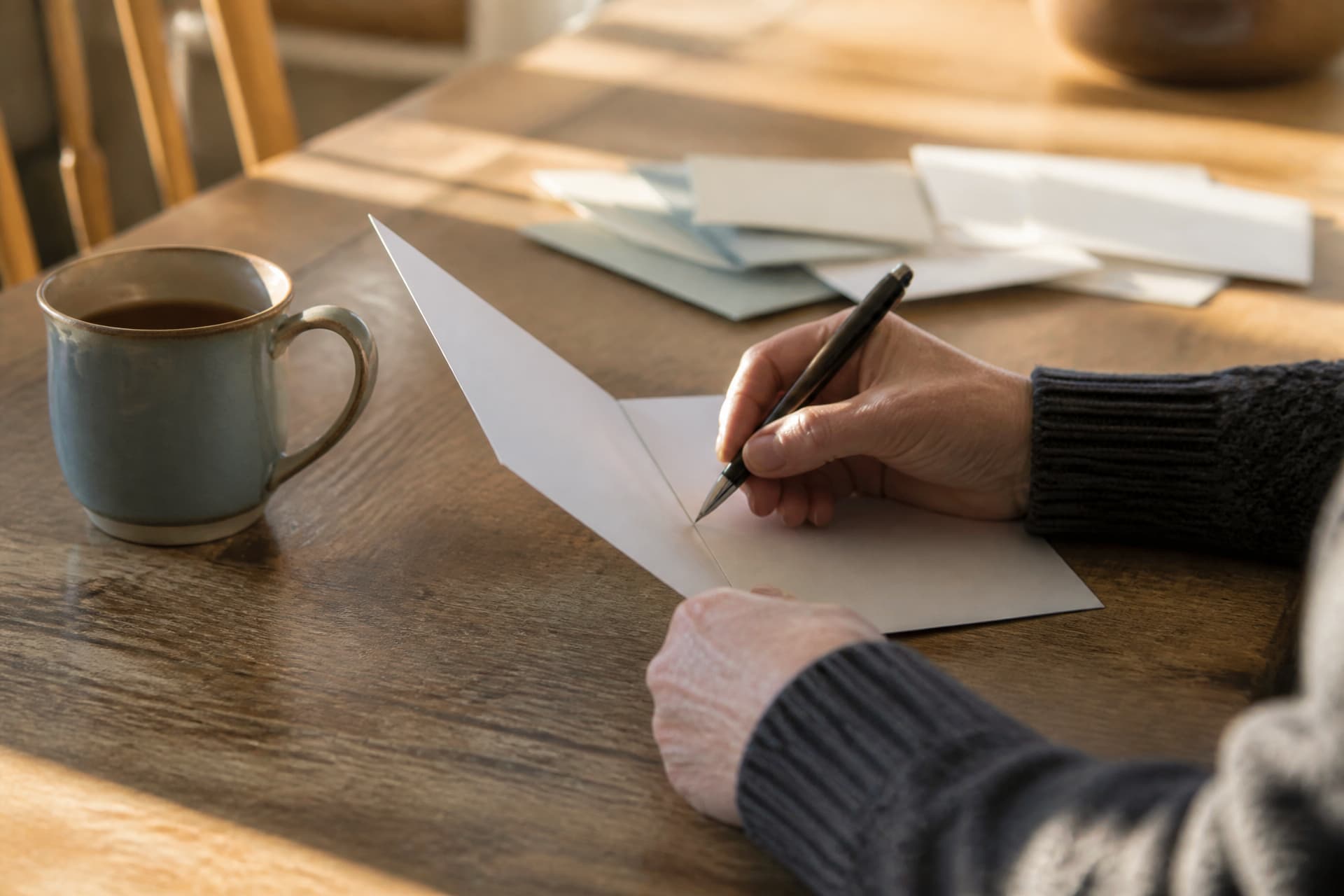 A person's hands writing in a sympathy card at a kitchen table, the card angled away from the camera