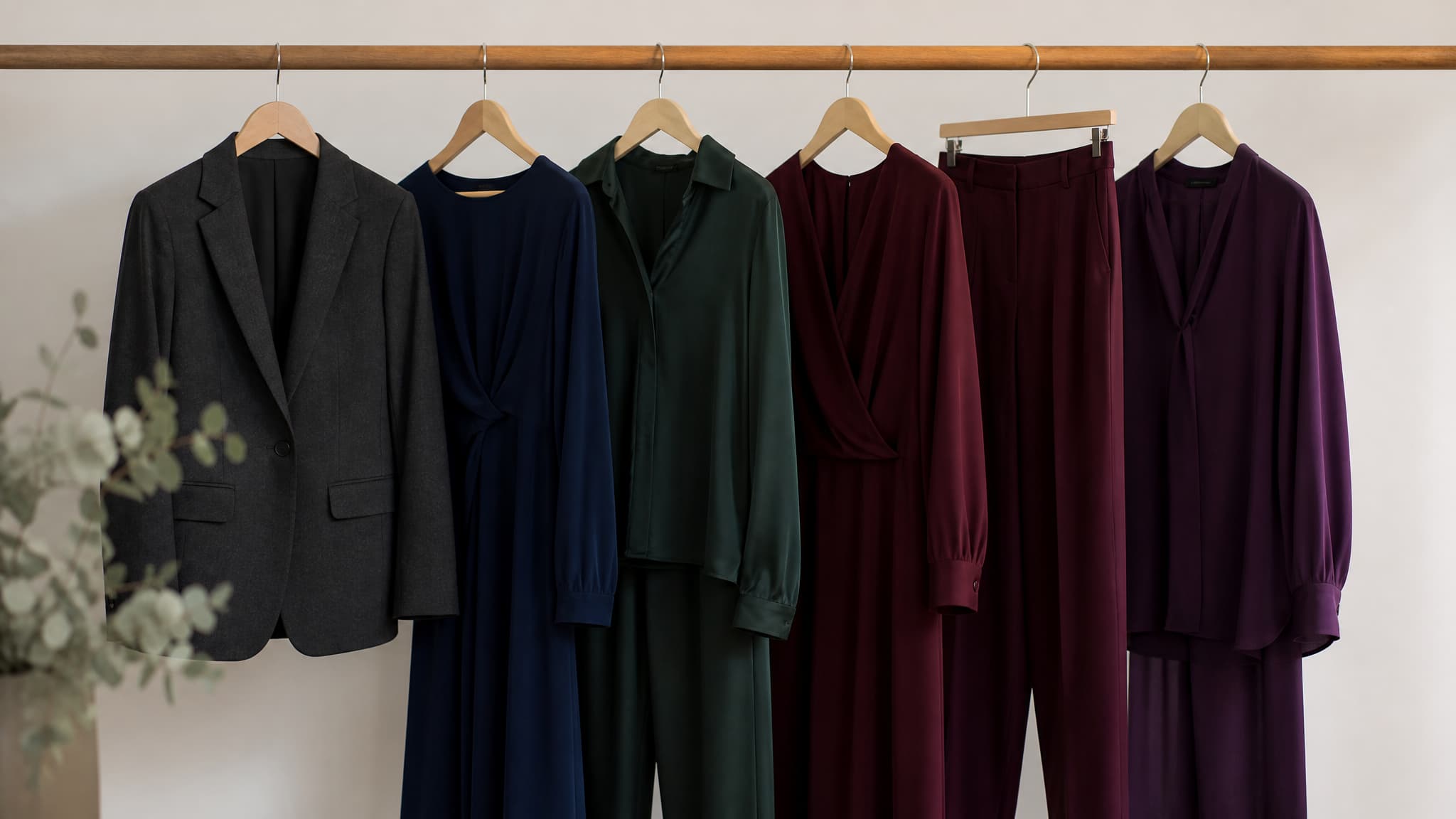 Dark garments in charcoal, navy, deep green and plum hanging together on a wooden rail