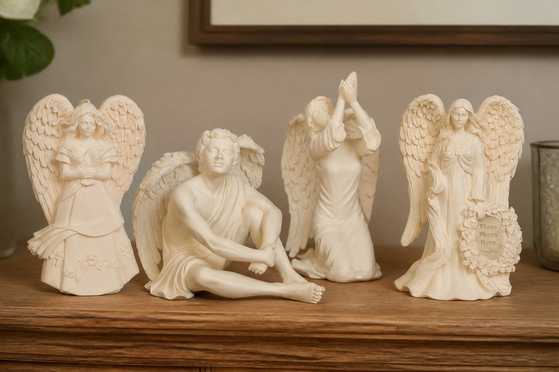 Four cast angel keepsakes on a wooden shelf in soft light โ a standing angel holding a book, a seated angel, a kneeling angel with hands raised, and a standing angel beside a small flower-edged photo frame