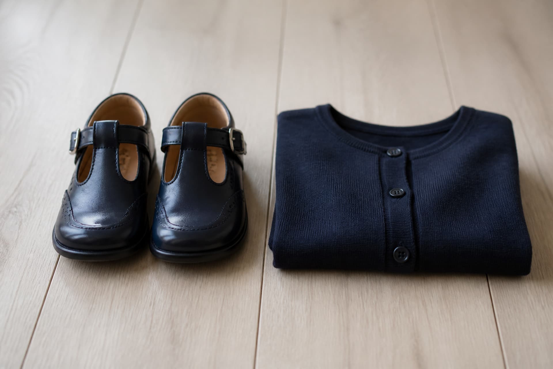 A pair of small polished dark shoes beside a neatly folded navy cardigan