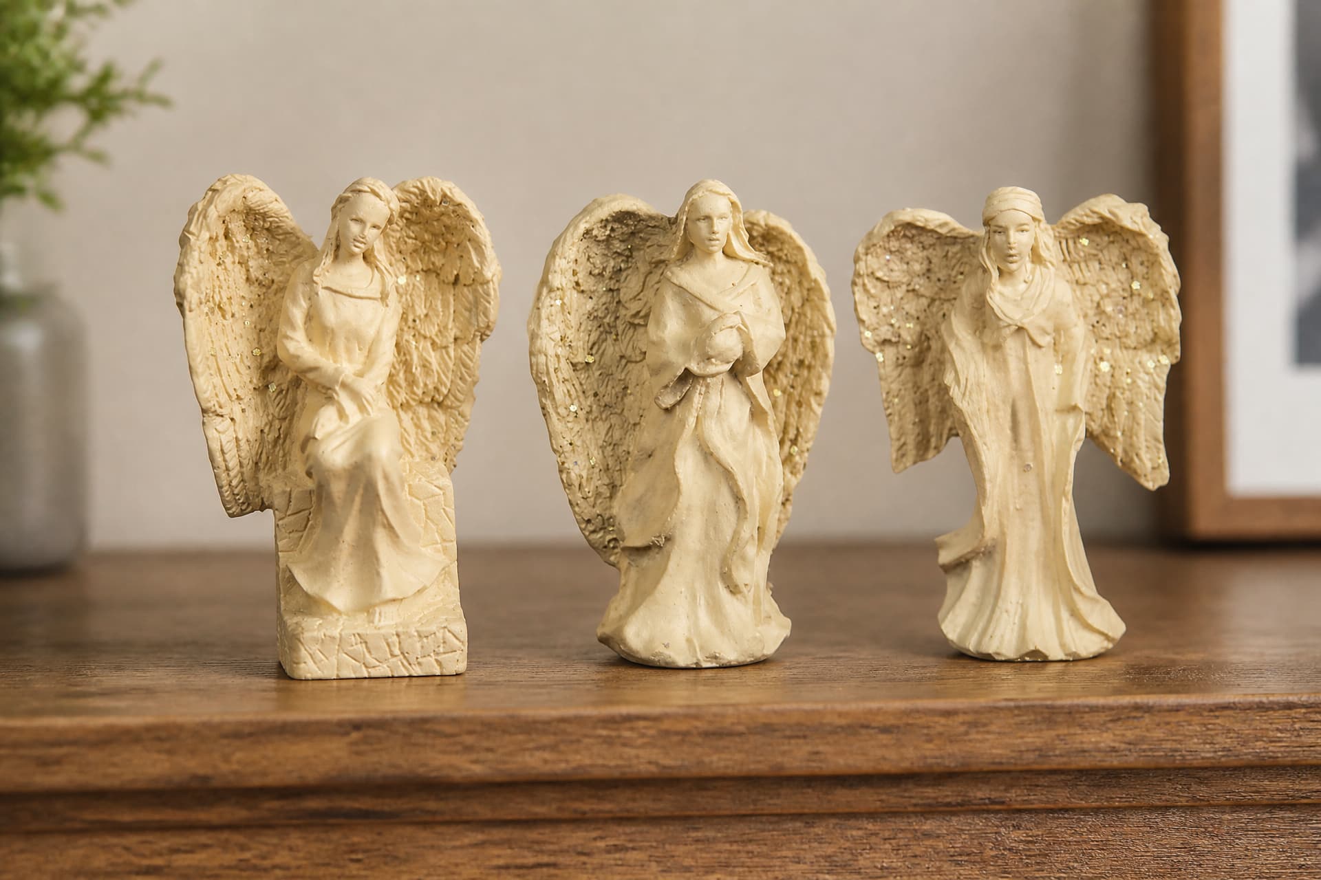 Three small cast stone angel figures with textured wings on a wooden shelf, one seated and two standing