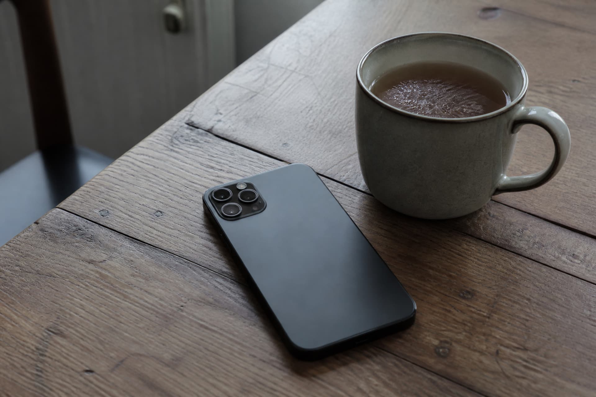 A phone lying face down on a wooden windowsill beside a cold mug of tea, low afternoon light through the glass