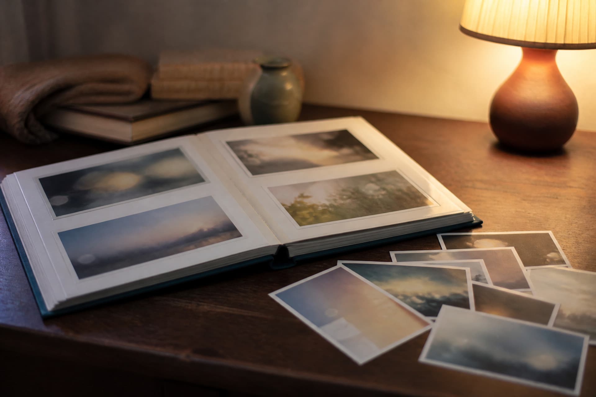 A printed photo album lying open on a table with several loose prints beside it, warm lamplight from the right